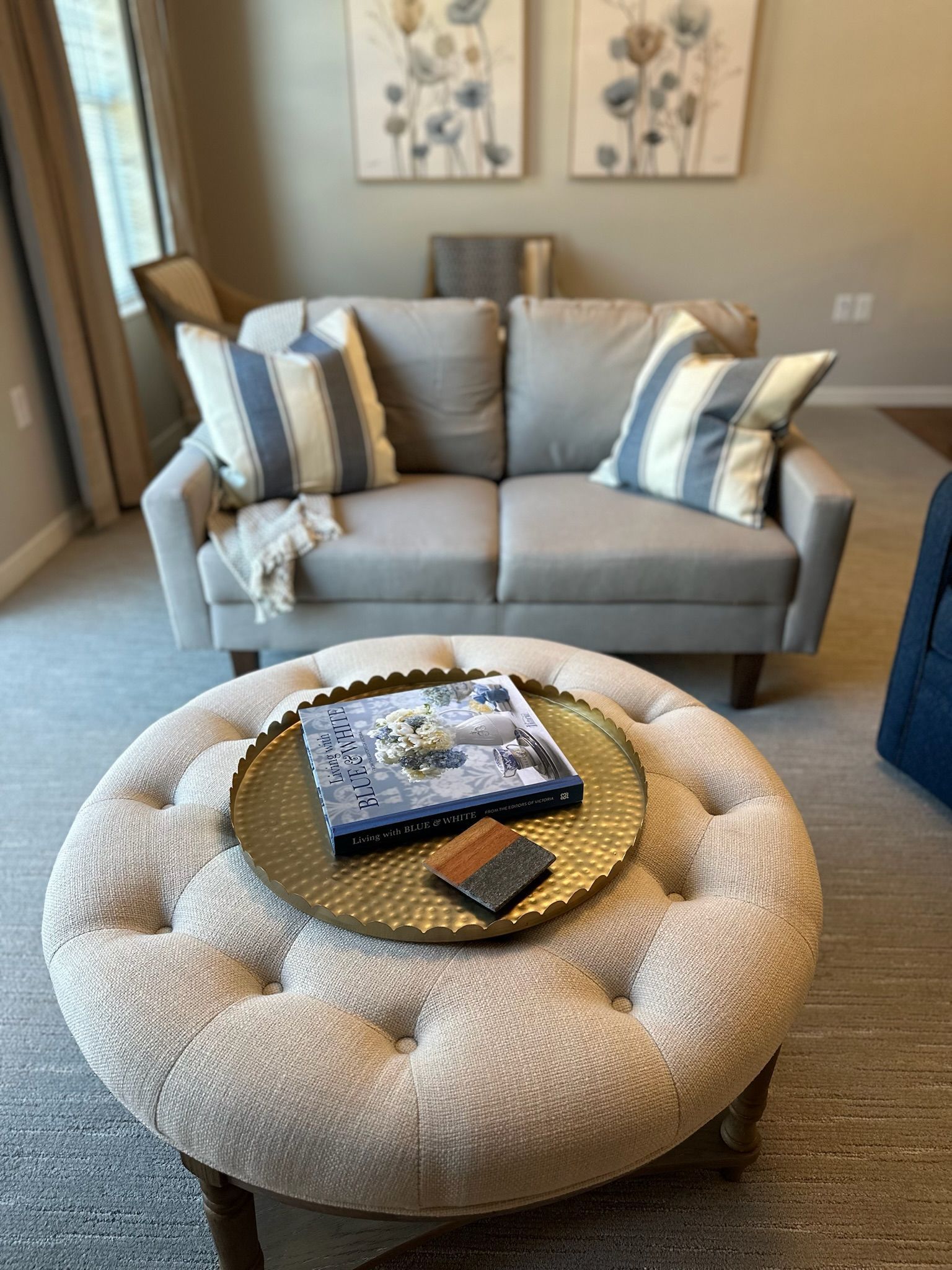 Cozy living room with a gray sofa, round tufted ottoman, and coffee tray in front of wall art.