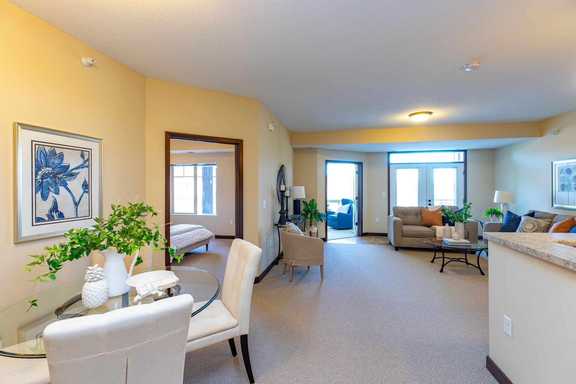 A dining area with a glass table and chairs flows into a bright living room with neutral decor and natural light.