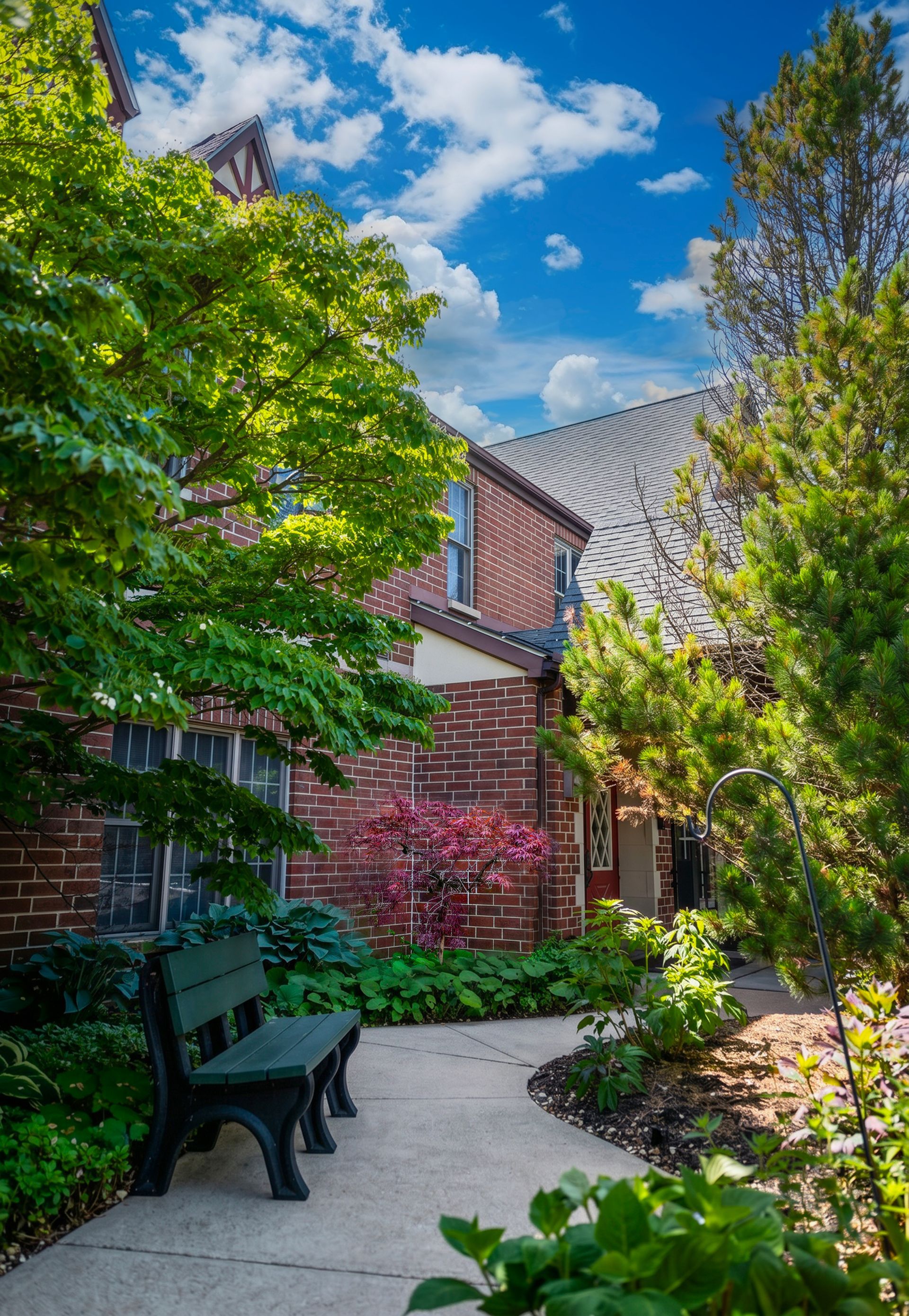 Leafy courtyard with a bench, brick building, and bright blue sky with clouds