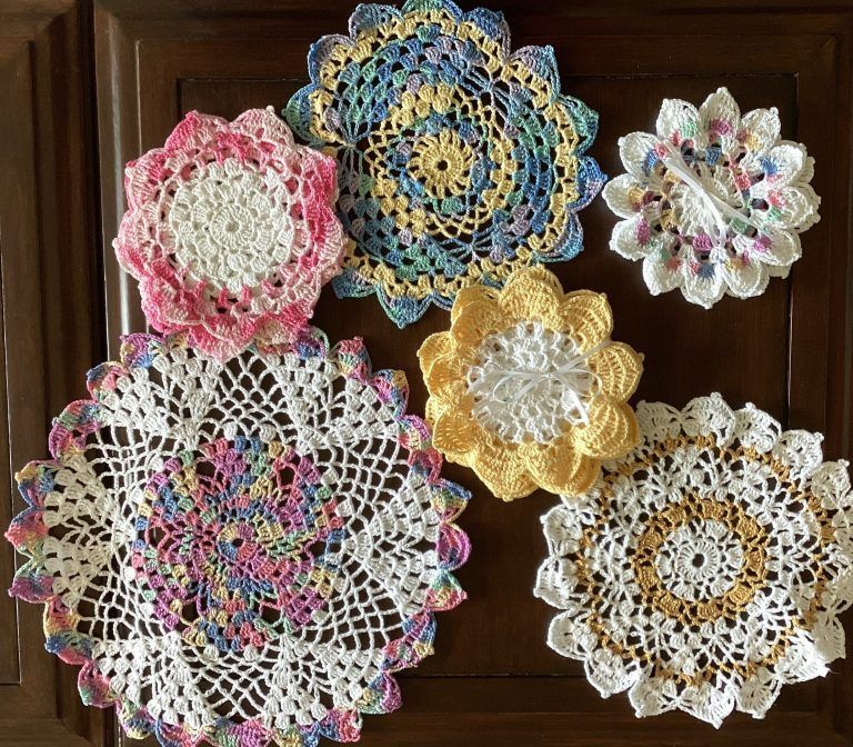 A collection of six colorful, handmade circular crochet doilies arranged on a dark wooden background.