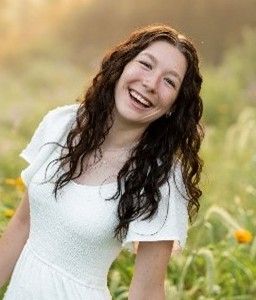 Smiling woman in a white dress standing in a grassy field with flowers