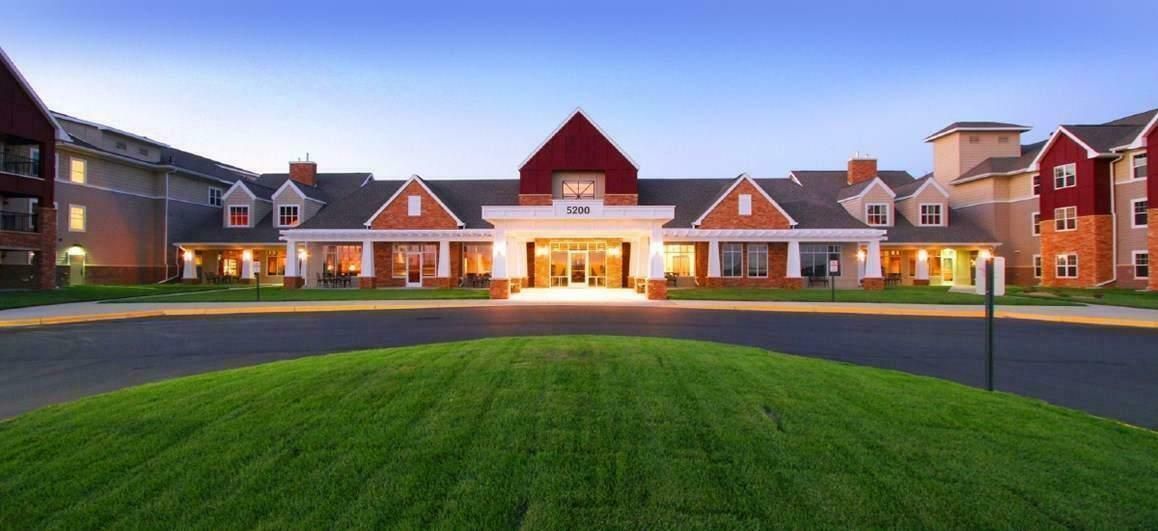 A low-rise, multi-wing building with a red-roofed central entrance and bright lighting, surrounded by a manicured lawn.