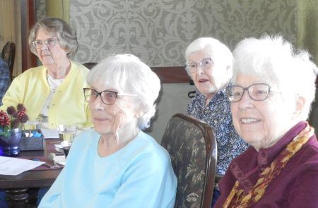 Four people sit together at a table indoors, engaged in conversation, with neutral expressions.