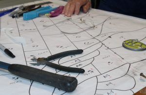 Tools and hand resting on a paper stencil with numbered sections, used for crafting a stained glass project.