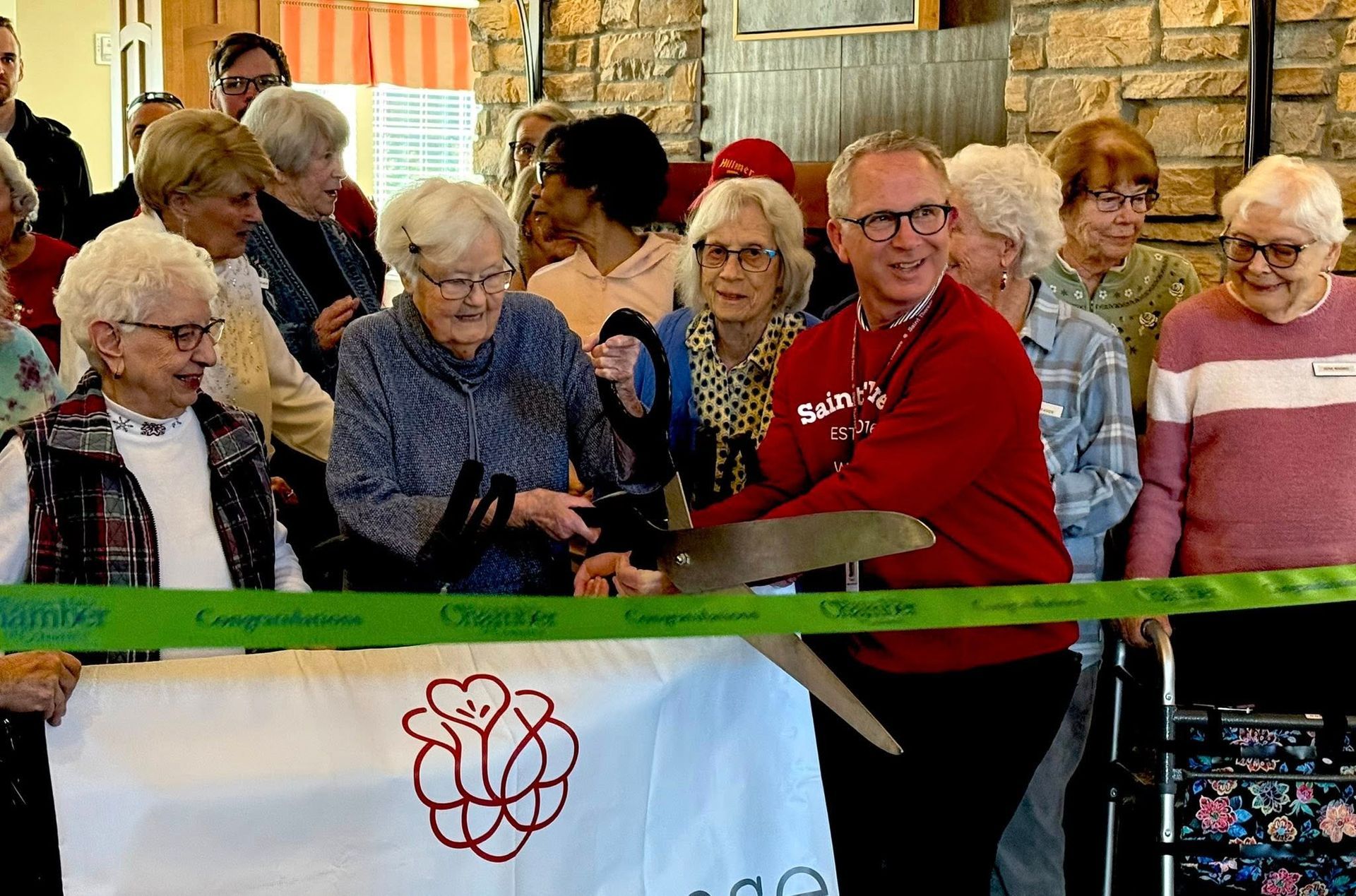 Group of people at a ribbon-cutting ceremony, standing behind a green ribbon and banner in an indoor setting