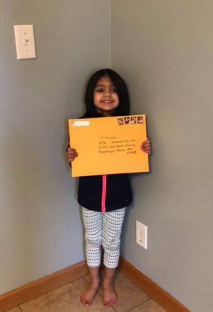 A person stands in a corner holding a yellow envelope with handwritten text.