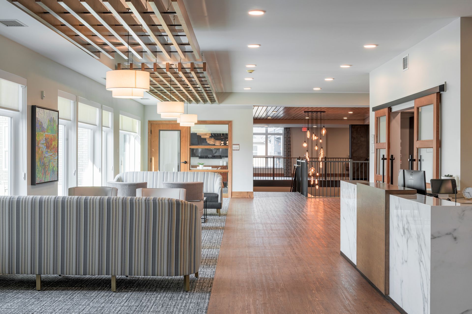 A modern hotel lobby with patterned sofas, a marble front desk, wood-slat ceiling accents, and warm ambient lighting.