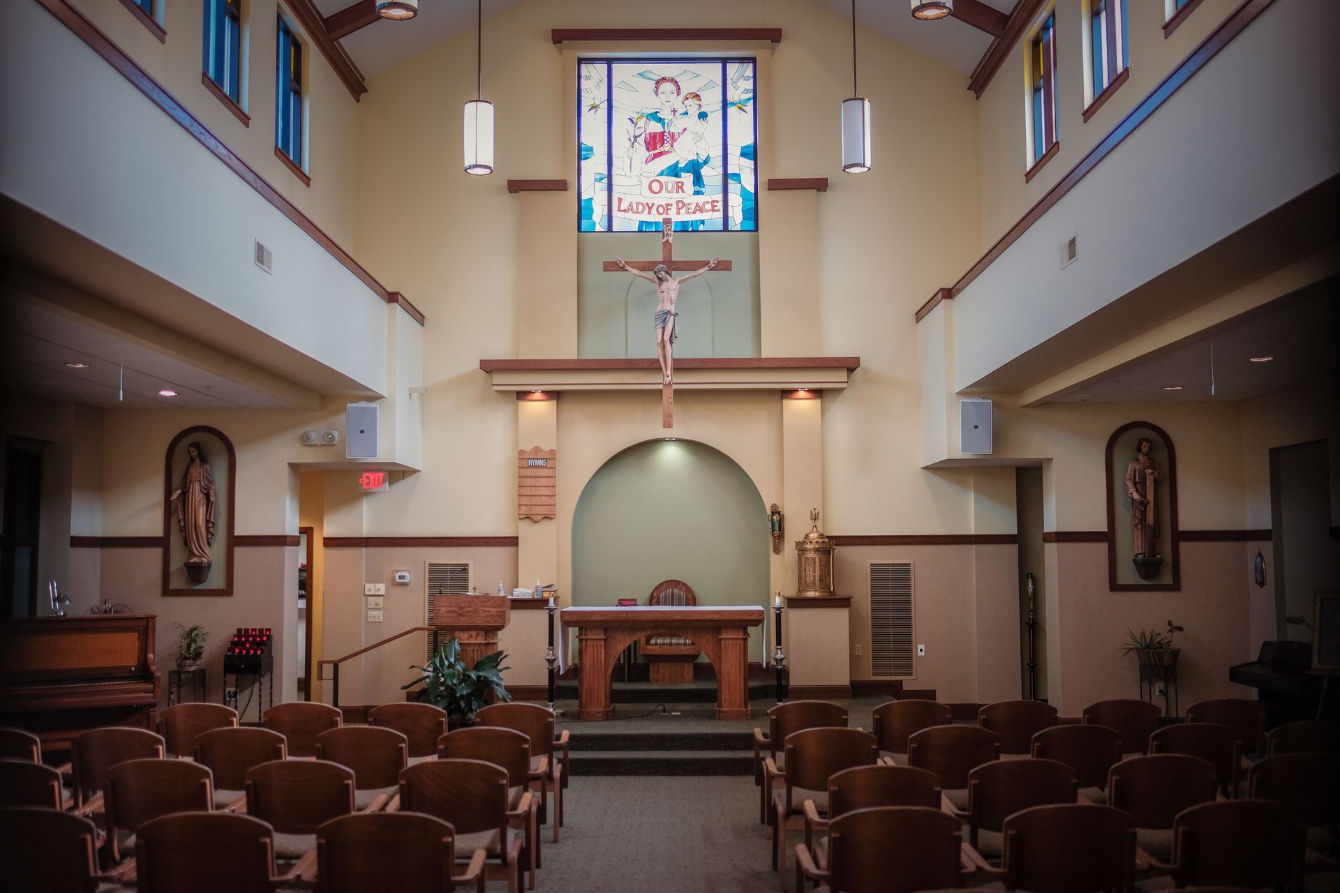 The interior of a church with rows of wooden chairs facing an altar, a crucifix, and a stained-glass window.
