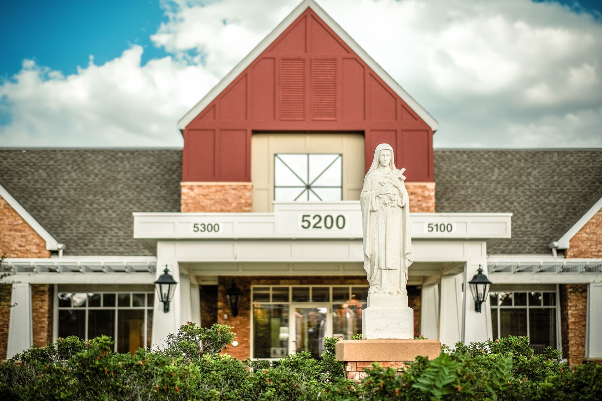A brick building with a pointed roof, white entryway, and a statue in front marked with the number 5200.