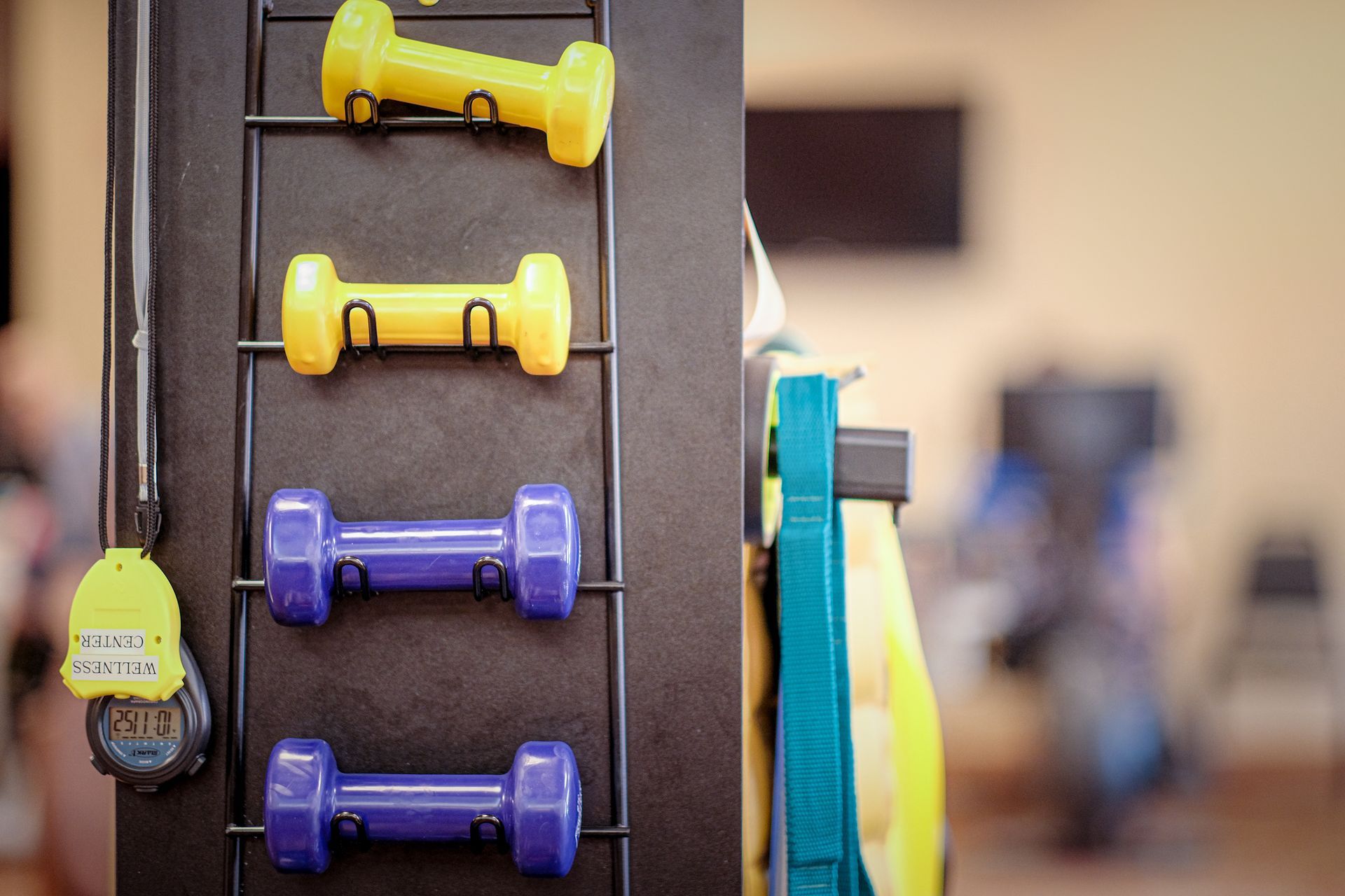 Dumbbells stored on a vertical rack in a gym, with a stopwatch hanging on the side.