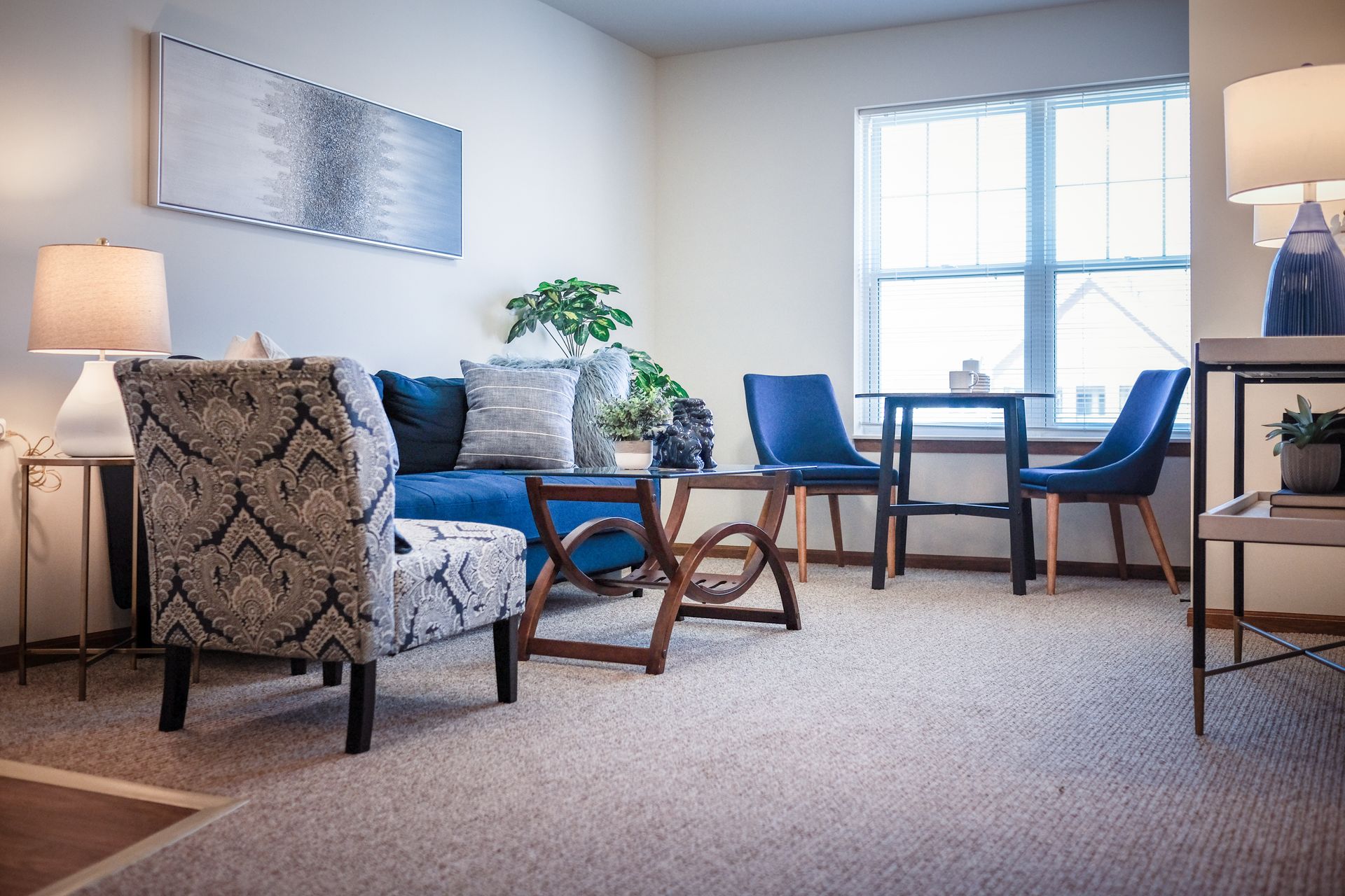 A modern living room with a patterned armchair, blue sofa, and a small dining set with two chairs near a window.