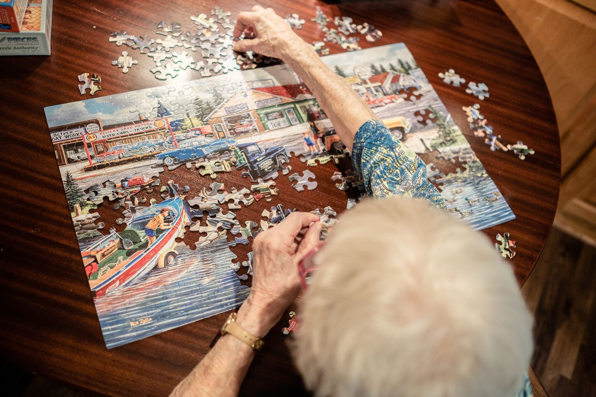 Hands working on a detailed jigsaw puzzle featuring a vintage town scene on a dark wooden table.