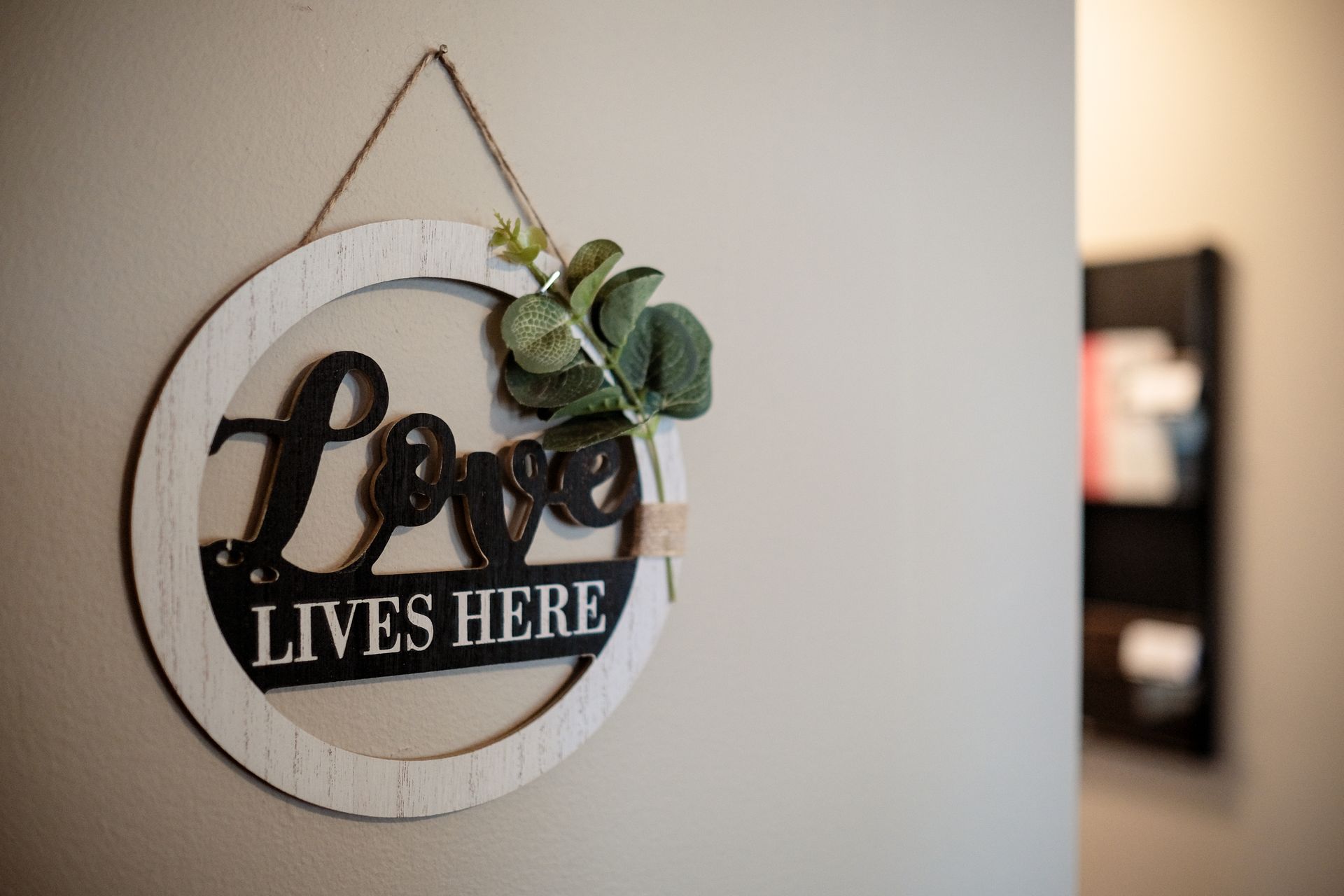 A circular wooden sign hangs on a light-colored wall, featuring the words 
