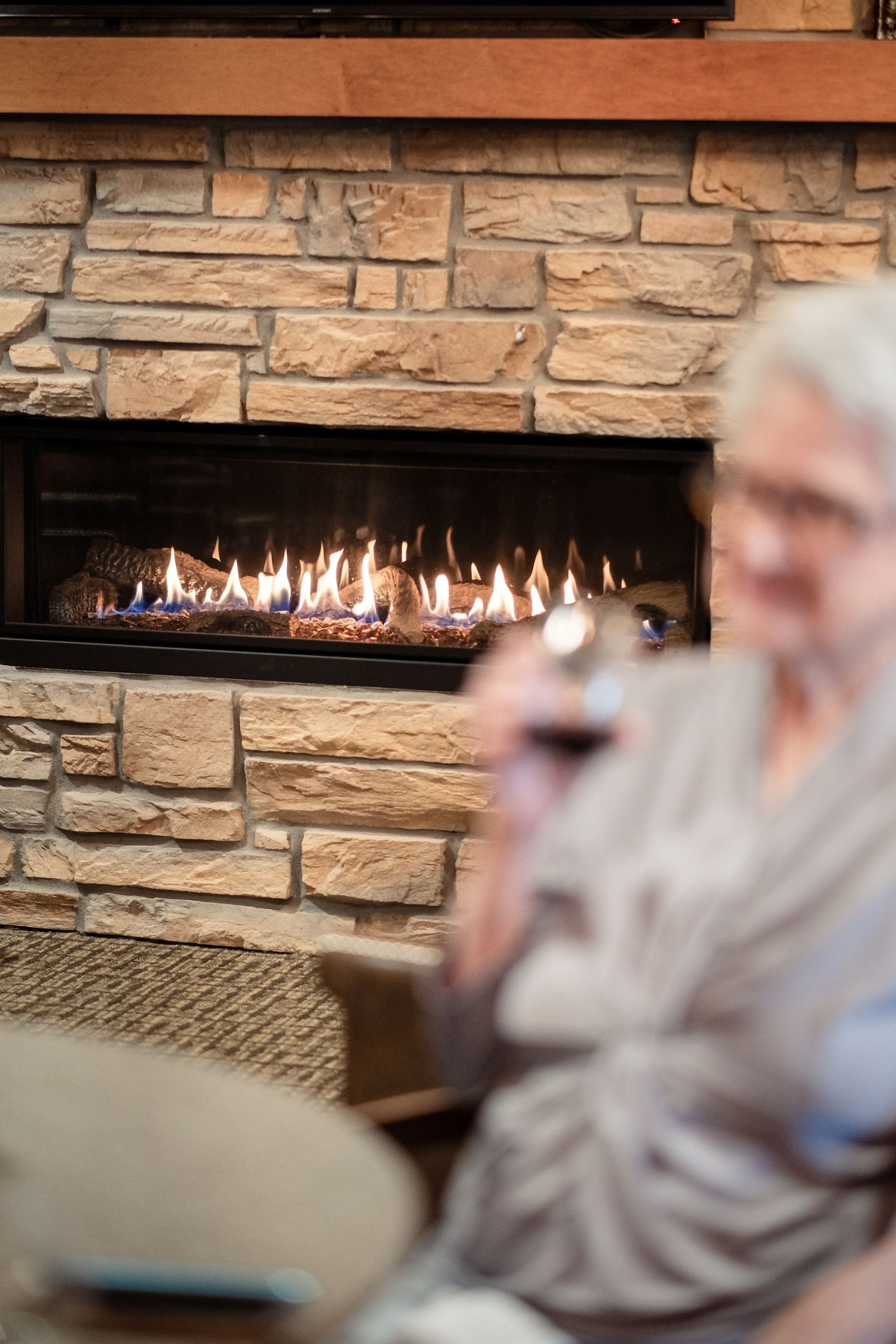 An out-of-focus person sits in front of a modern linear fireplace with stacked stone surround.