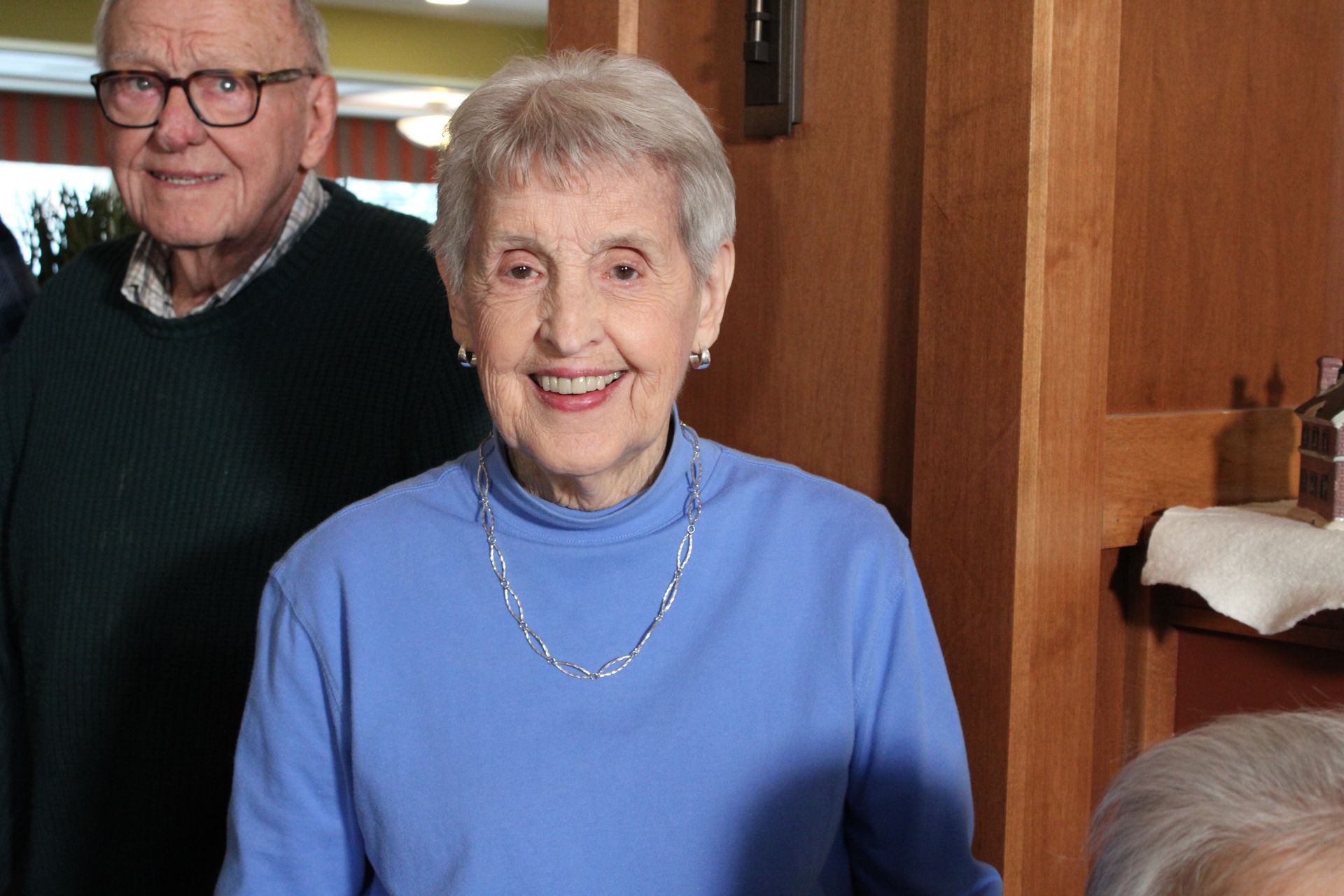 Smiling older couple standing indoors, with wood paneling in the background.