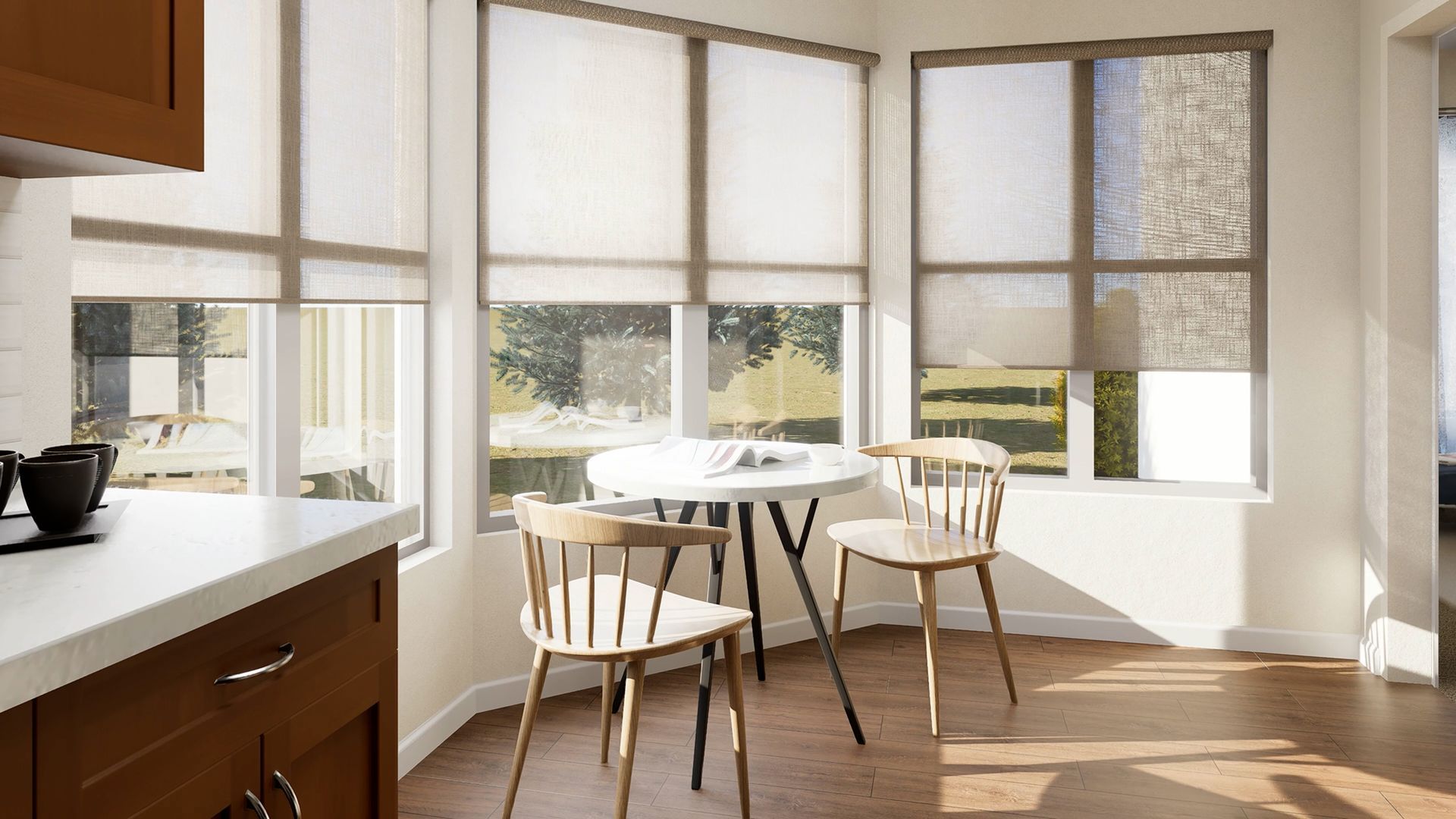 A sunlit breakfast nook with a small round table, two wooden chairs, and windows with neutral roller shades.