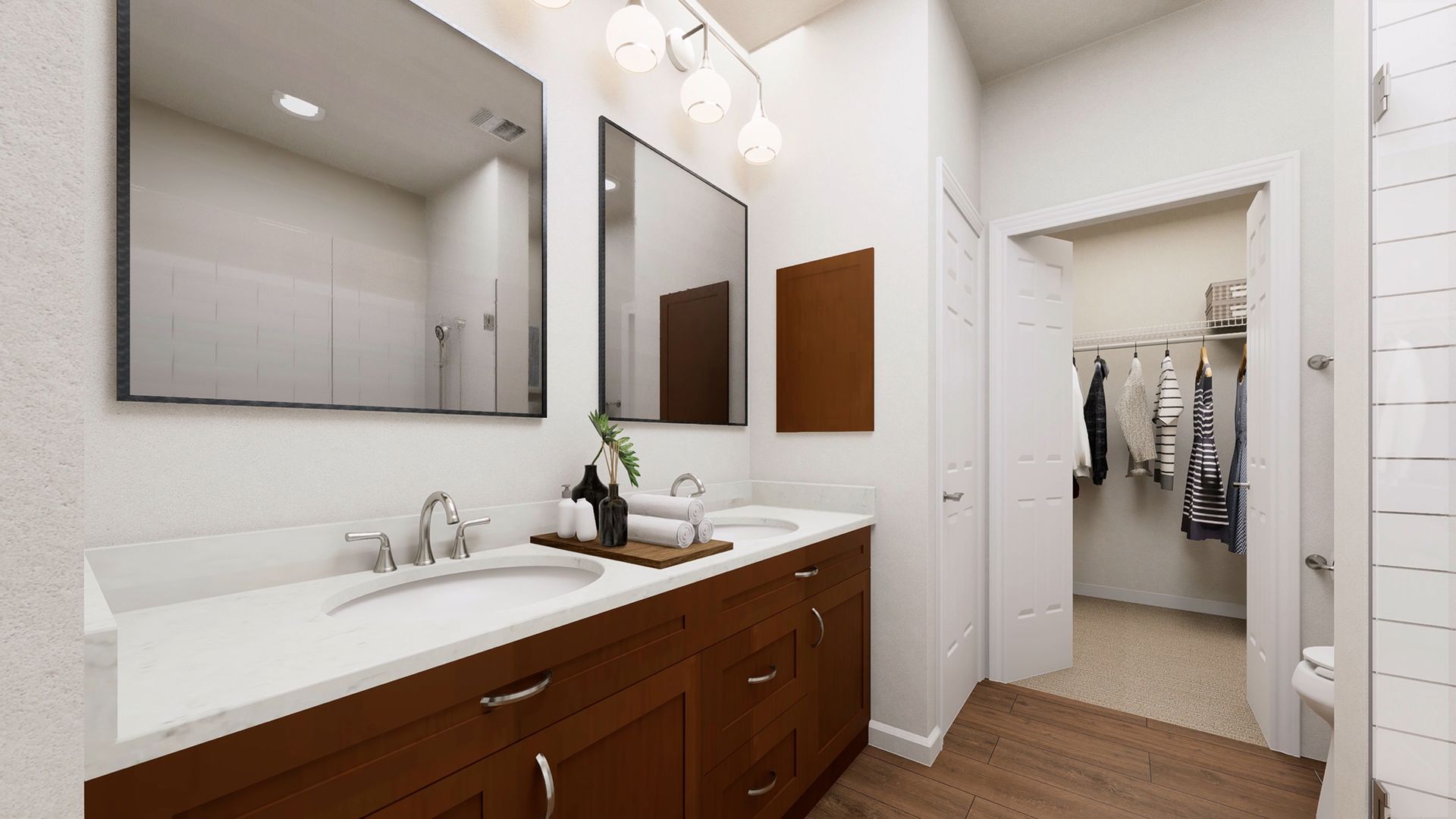 A bathroom with a double wood vanity, white countertops, two large mirrors, and an open doorway to a walk-in closet.