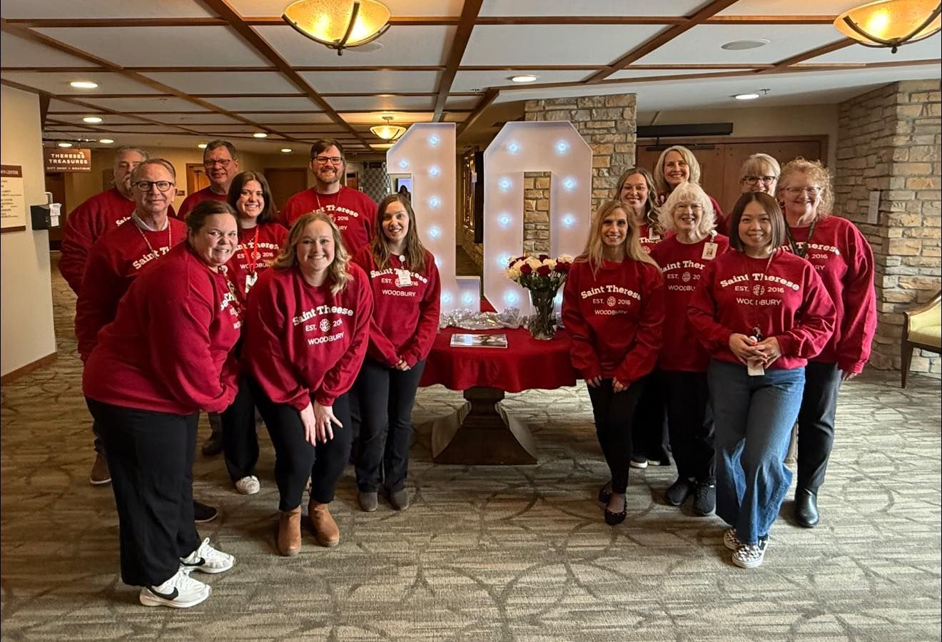 Group in matching red sweatshirts posing indoors at a holiday event with a decorated table and stone wall backdrop