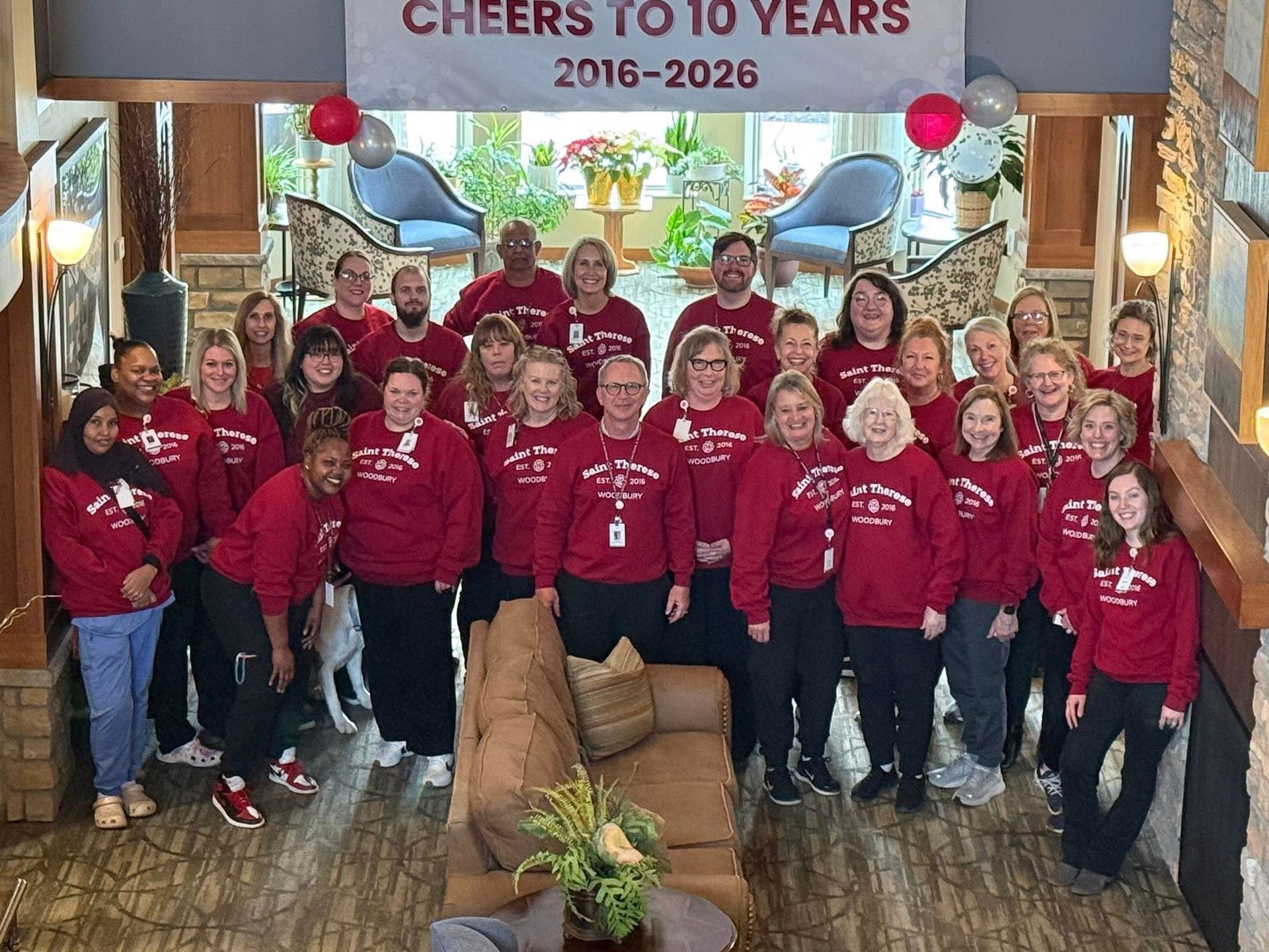 Group in red shirts posing indoors beneath a “Cheers to 10 Years 2016–2026” banner.