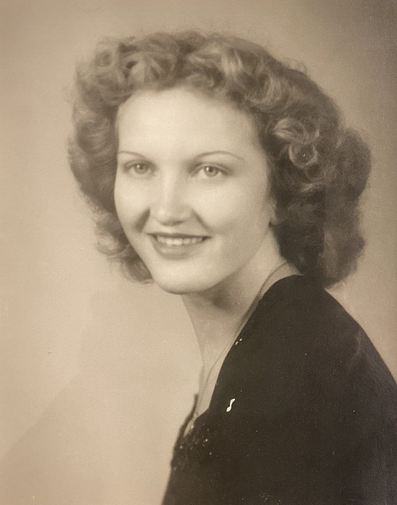 Portrait of a person with wavy hair, smiling softly, wearing a dark top against a neutral background in vintage style.