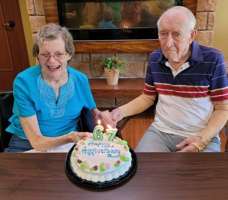 A smiling couple holds hands over a cake with lit candles that says 
