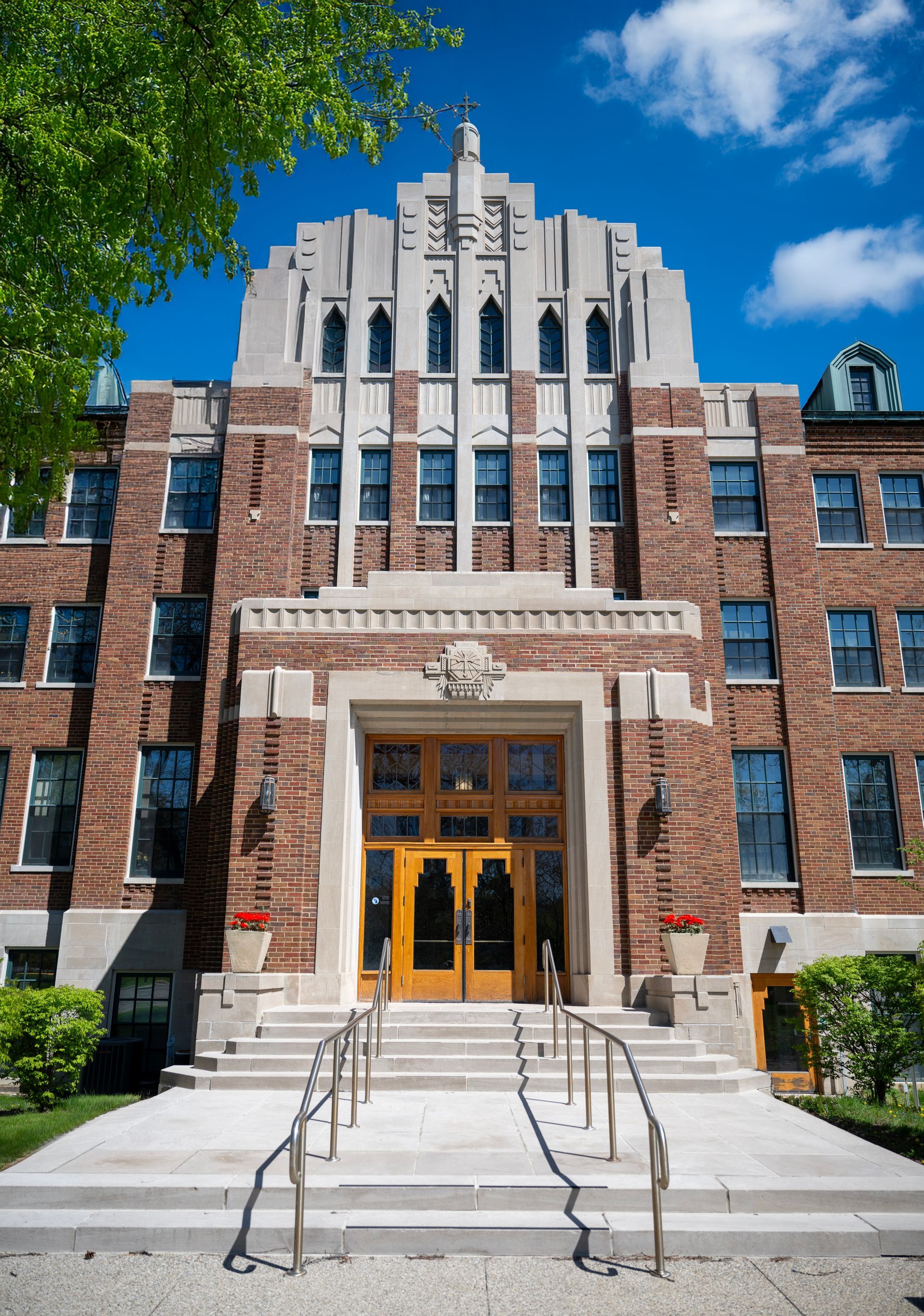 Historic brick building with ornate stone entrance, central steps, and tall arched windows under a blue sky