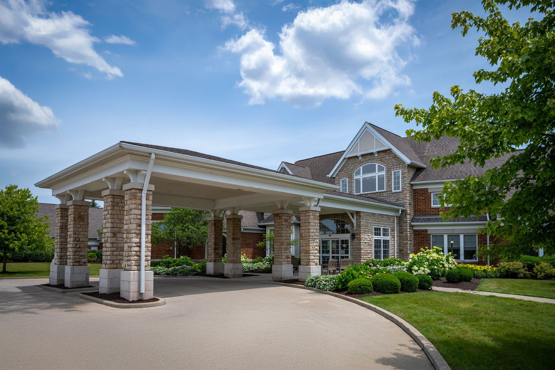 A large, multi-story brick building with a stone-columned porte-cochère entrance under a bright blue sky.