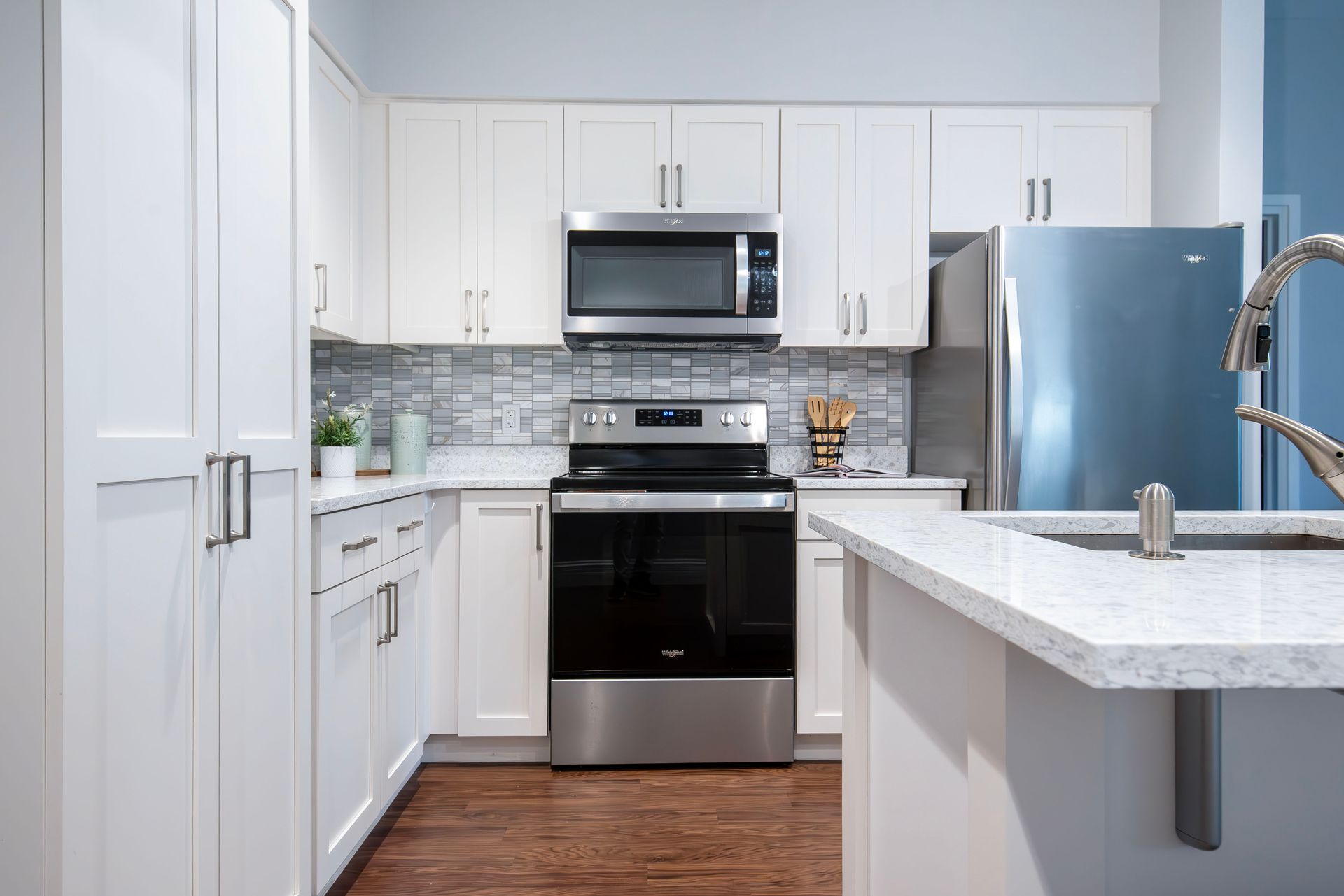 Modern white kitchen with stainless steel appliances, marble island, and hardwood floor