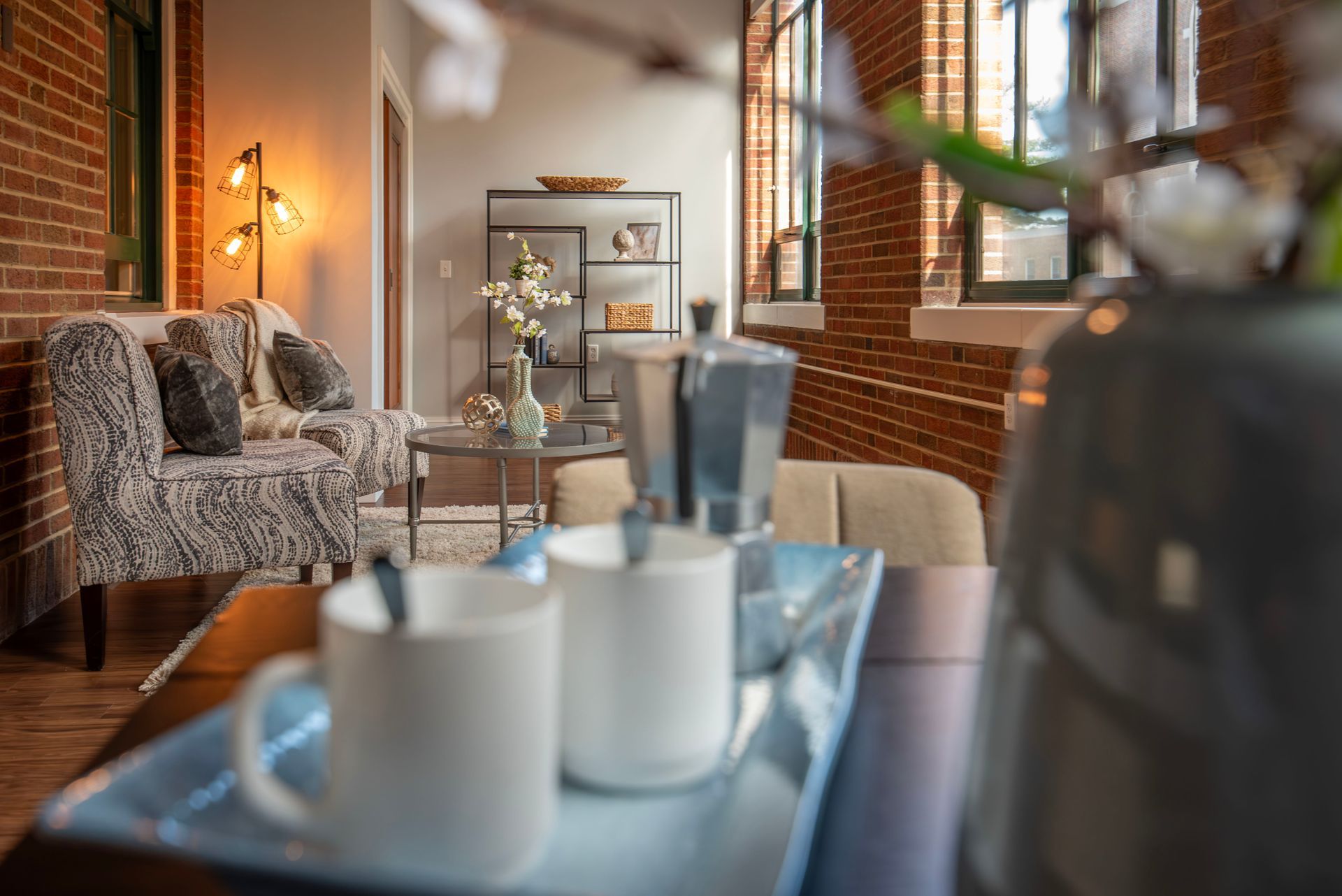 Cozy café lounge with patterned sofa, brick walls, warm lighting, and a tray of coffee cups in the foreground