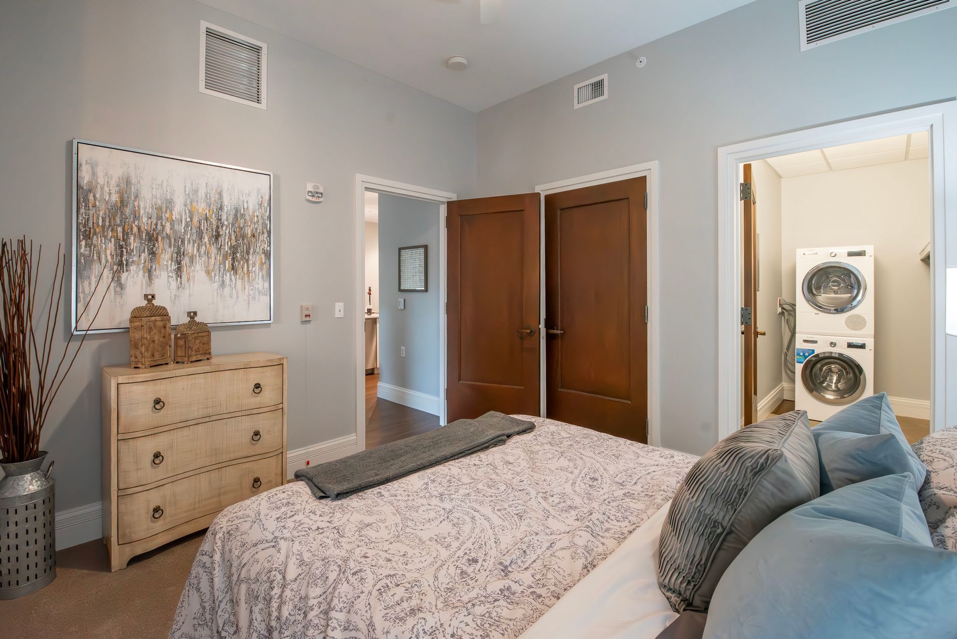 Cozy bedroom with patterned bedding, dresser, wall art, and double closet doors.