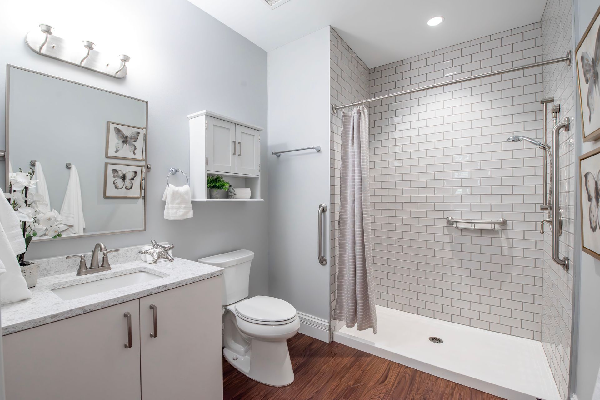 Bright modern bathroom with white vanity, toilet, and glass walk-in shower over wood-look flooring
