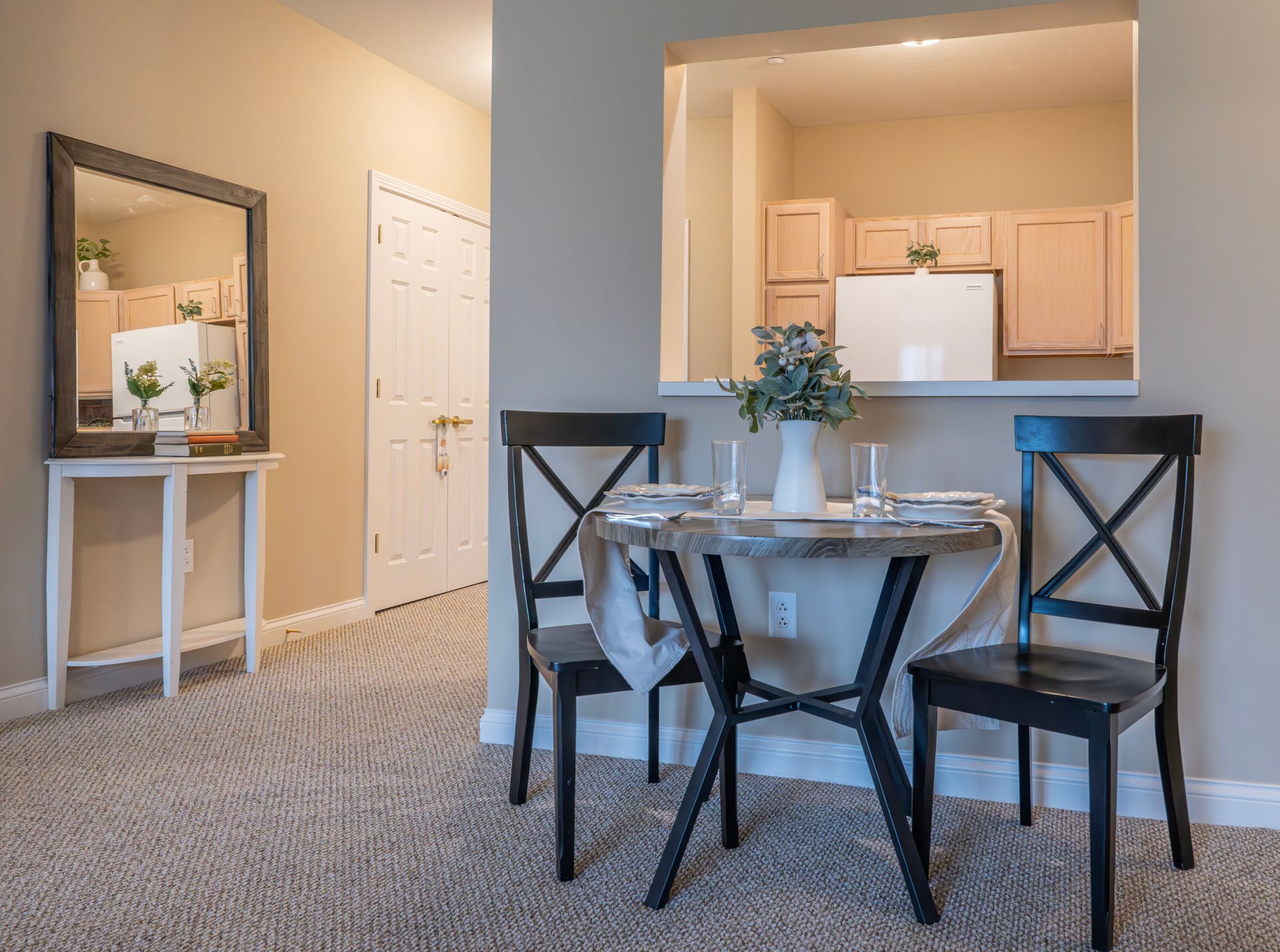 A dining area featuring a round table with two black chairs, positioned in front of a kitchen pass-through window.