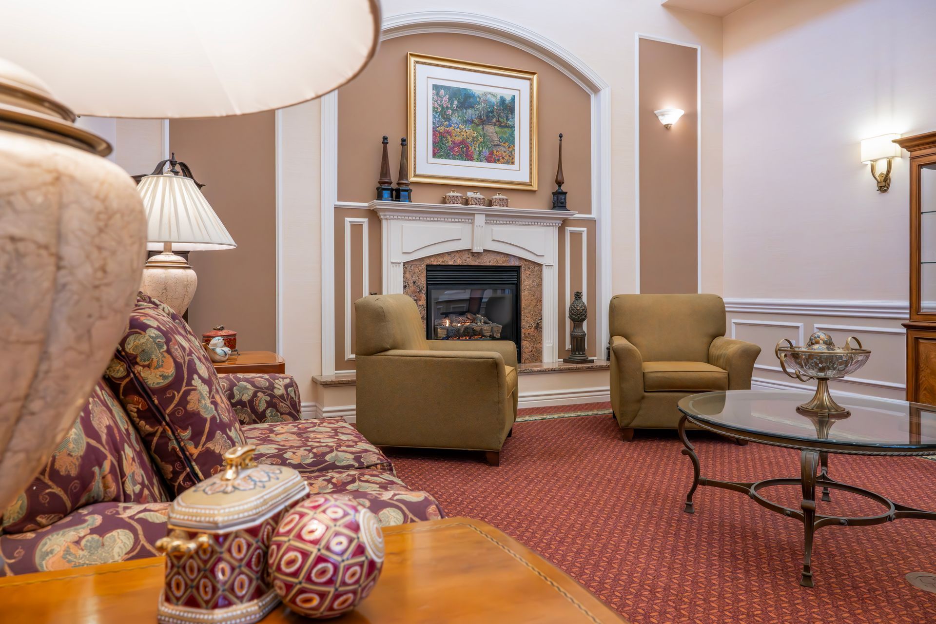 Cozy living room with fireplace, floral sofa, two armchairs, and glass coffee table
