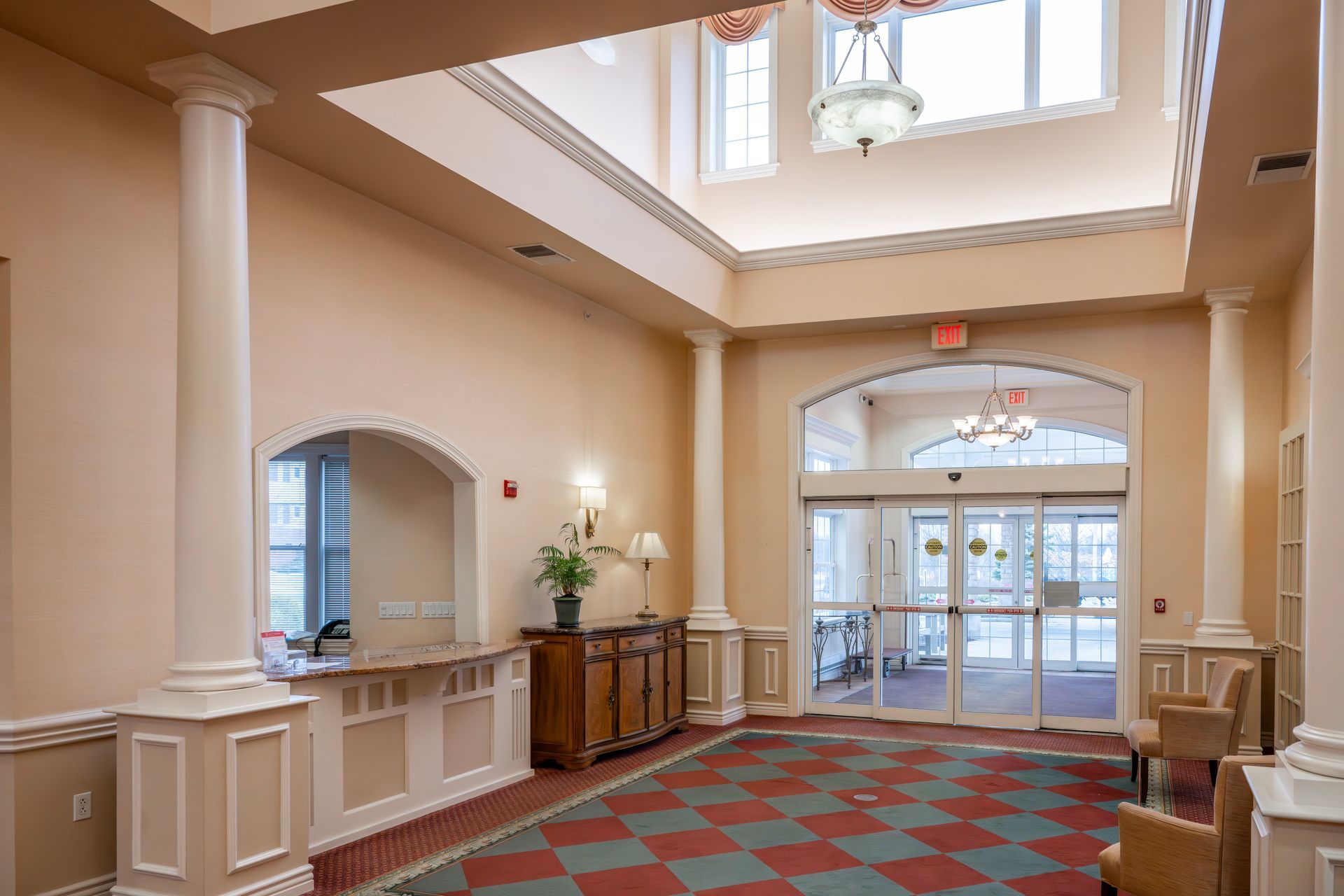 A lobby with high ceilings, columns, a reception desk, a tiled floor in a diamond pattern, and glass entrance doors.