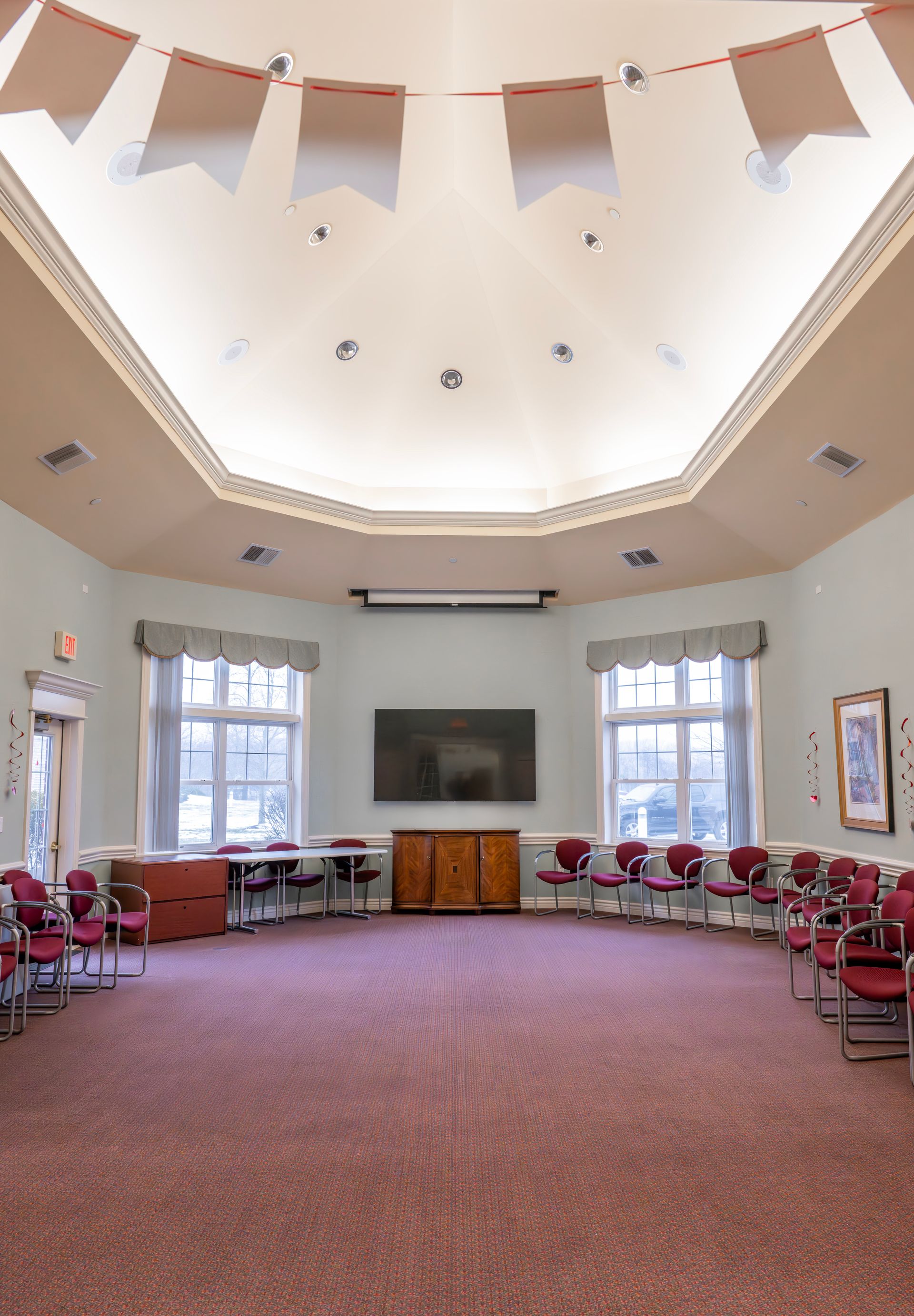 A spacious, circular room with light walls, red carpeting, a vaulted ceiling with banners, and chairs arranged in a circle.