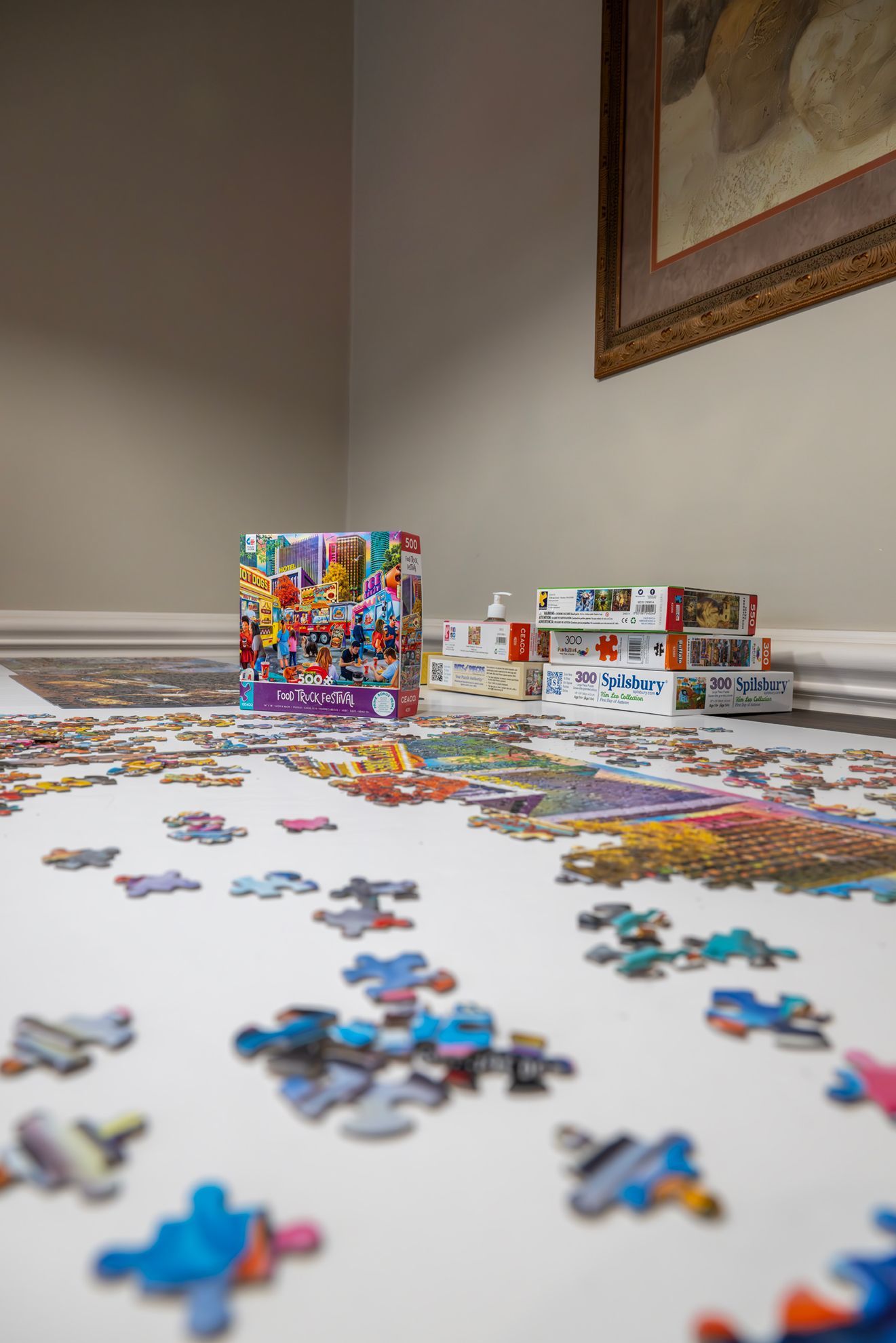 Jigsaw puzzle pieces scattered on a floor with the puzzle box and a stack of boxes in the background.
