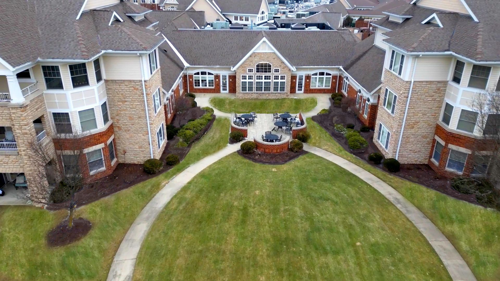 Aerial view of a U-shaped apartment building with a central courtyard, stone and brick facade, and green lawn pathways.