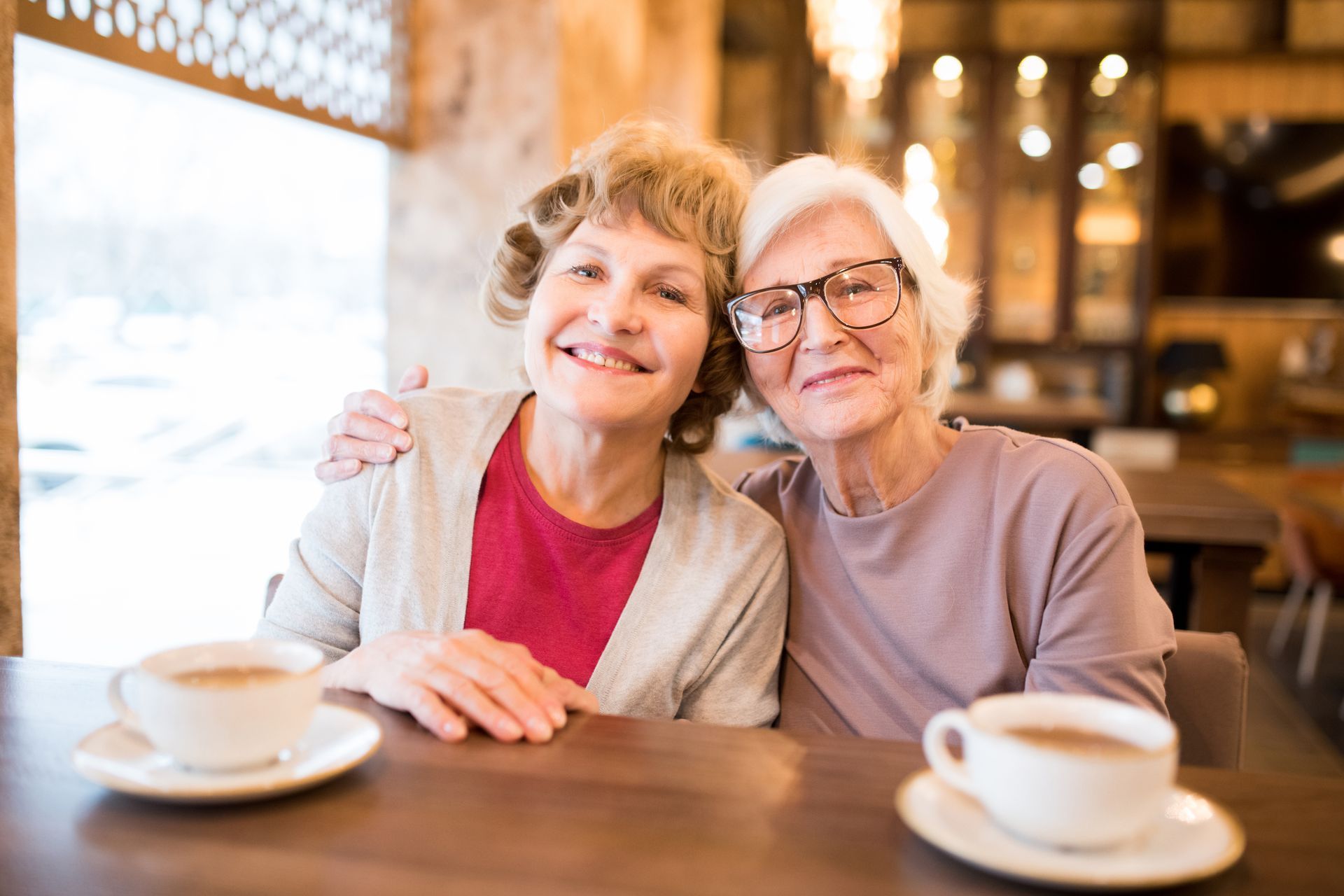 Two people sitting at a cafe table with coffee cups, smiling and posing for a photo.