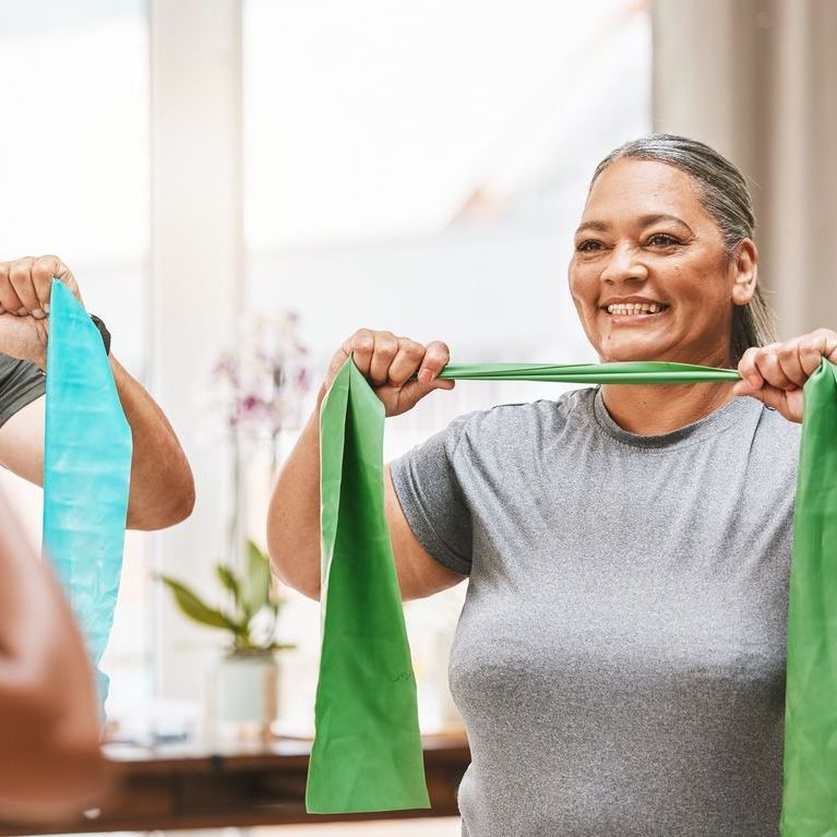 A smiling person holding a green resistance band horizontally in front of their chest during an exercise class.