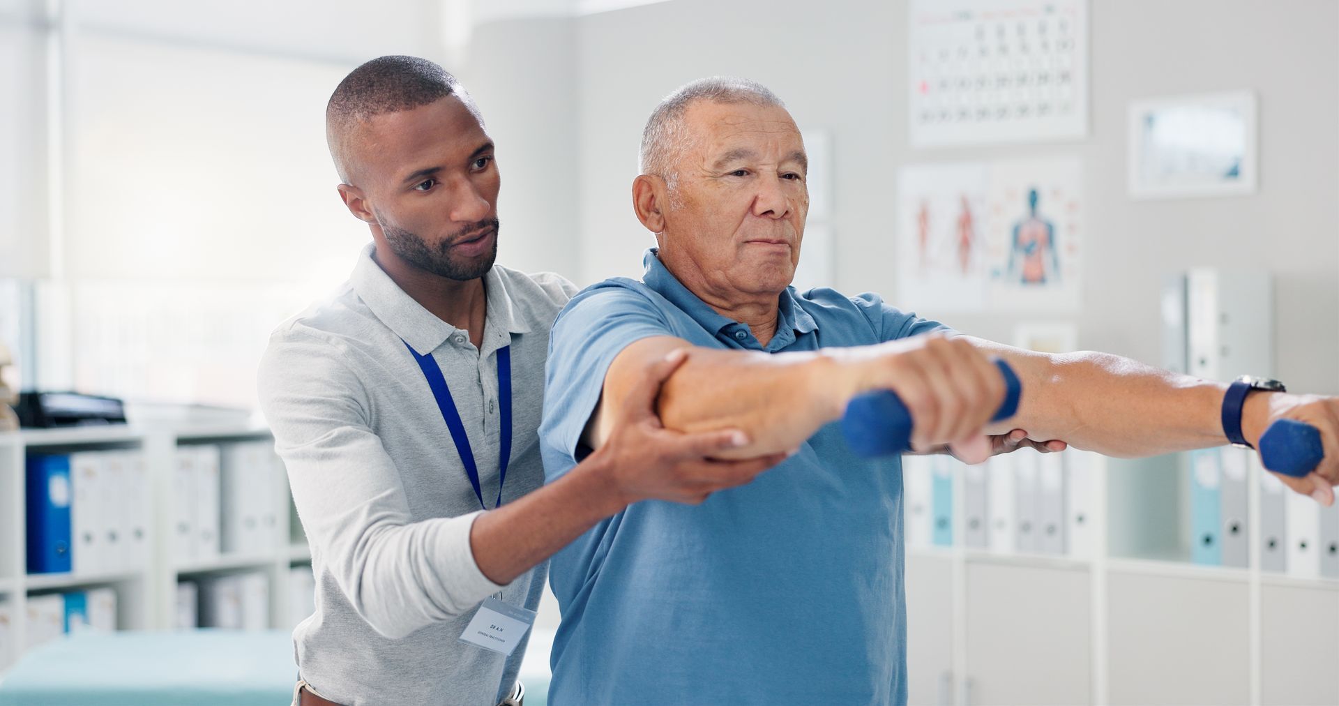 A physical therapist helps a person lift small blue hand weights in a brightly lit medical office.