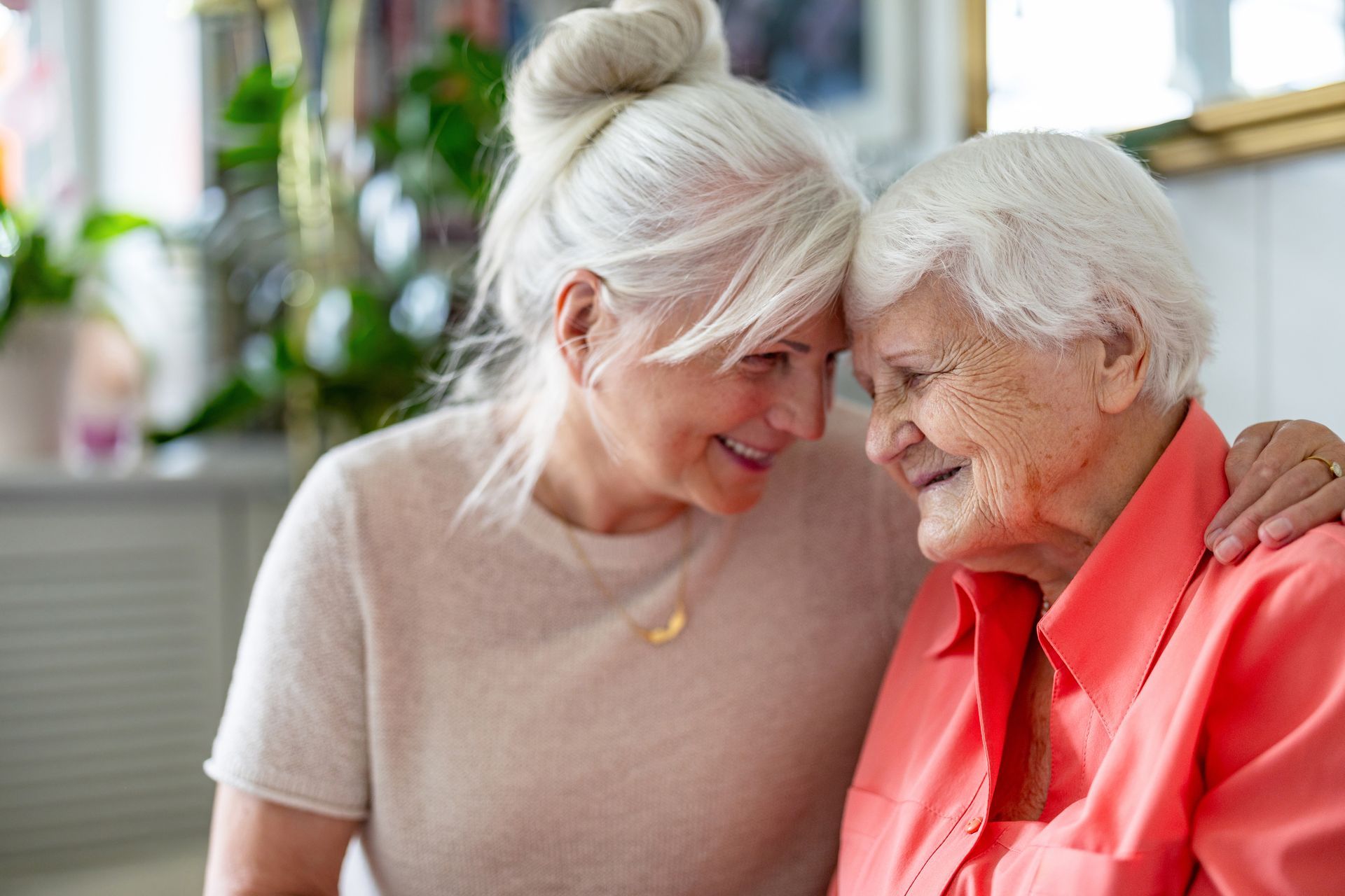 Two people with white hair lean their heads together affectionately, smiling.