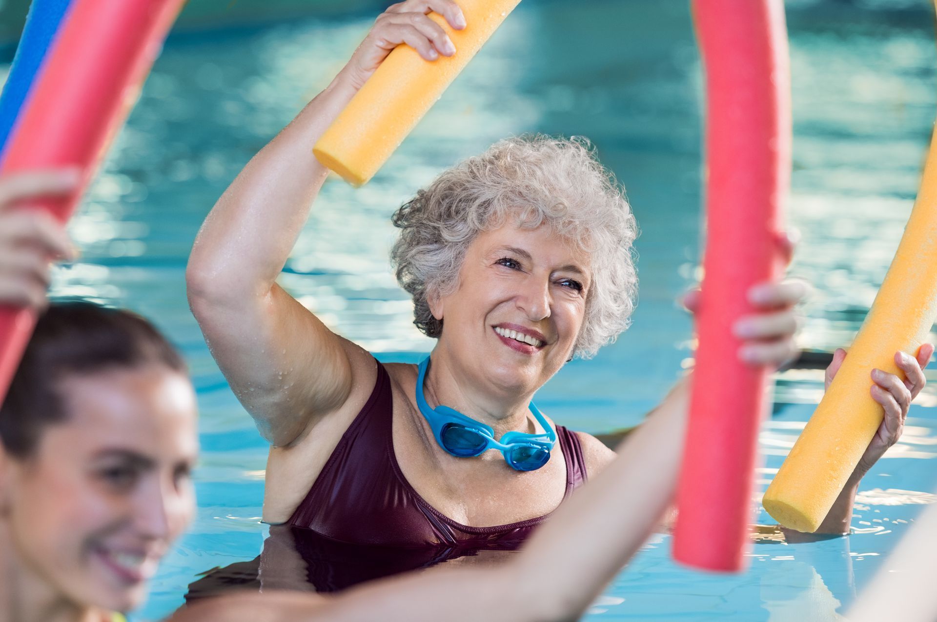People with smiles exercising in a pool using colorful foam water noodles.