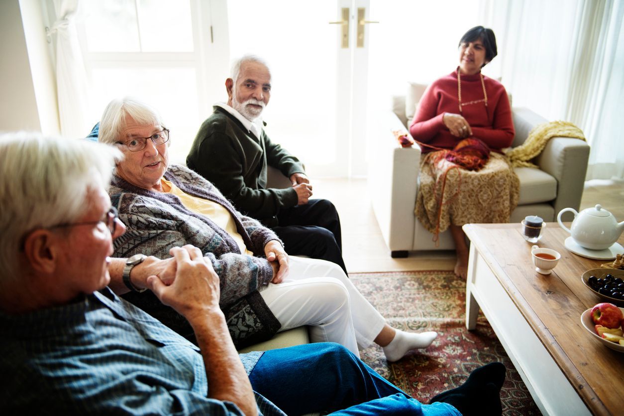 Four people sit in a bright living room, engaged in conversation while one person knits.