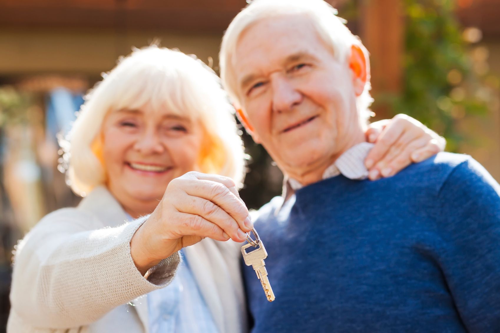 Smiling couple standing outdoors, holding up a silver house key towards the camera.