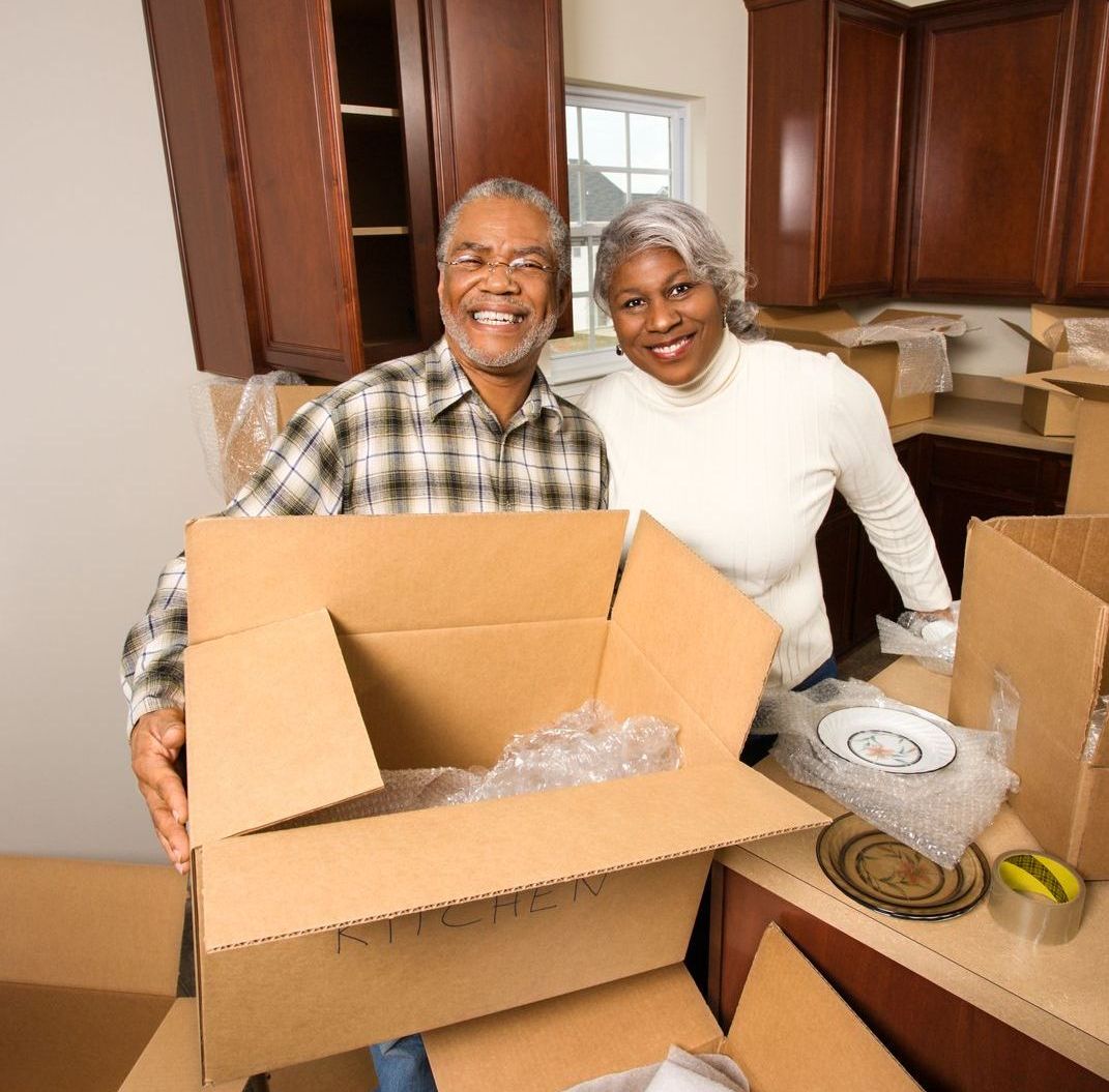 Two people smiling while packing cardboard boxes in a kitchen.