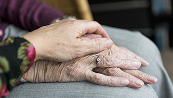 A hand with a silver ring rests on top of another pair of hands in a supportive gesture.