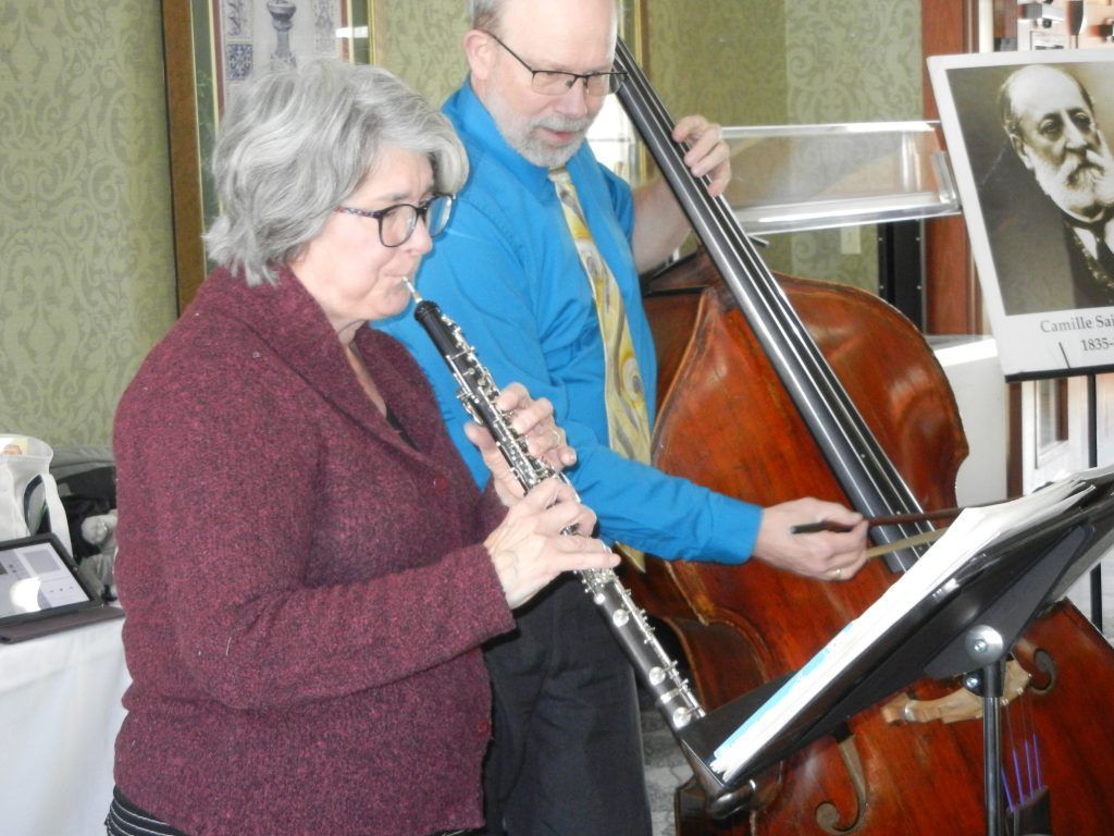 Two musicians, one playing an oboe and another playing a double bass, look at sheet music in an indoor setting.