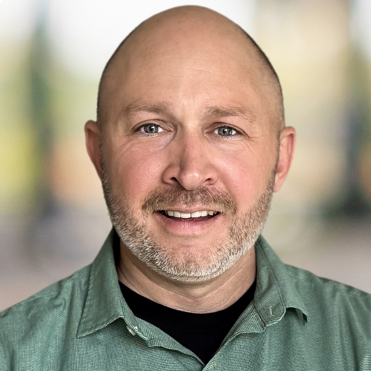 A bald man with a beard is wearing a green shirt and smiling for the camera.