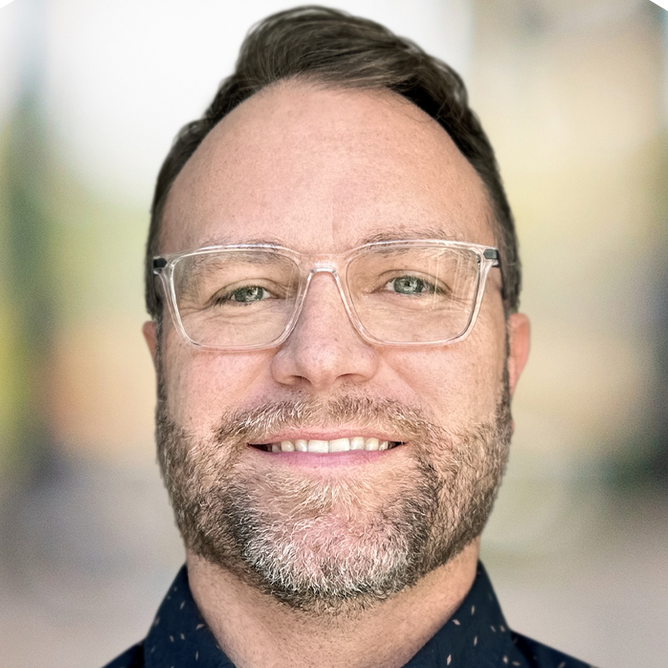 A man with glasses and a beard is smiling for the camera.