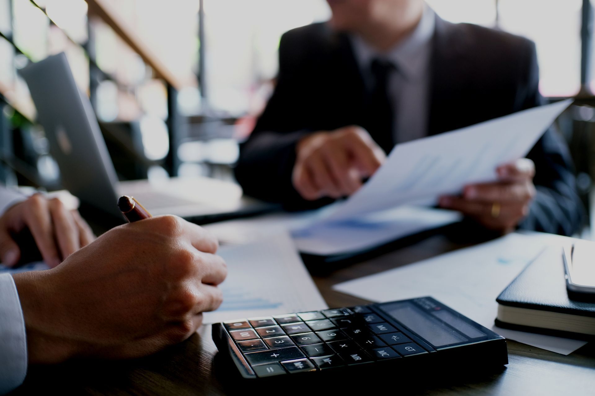 Two men are sitting at a table with a calculator and papers.
